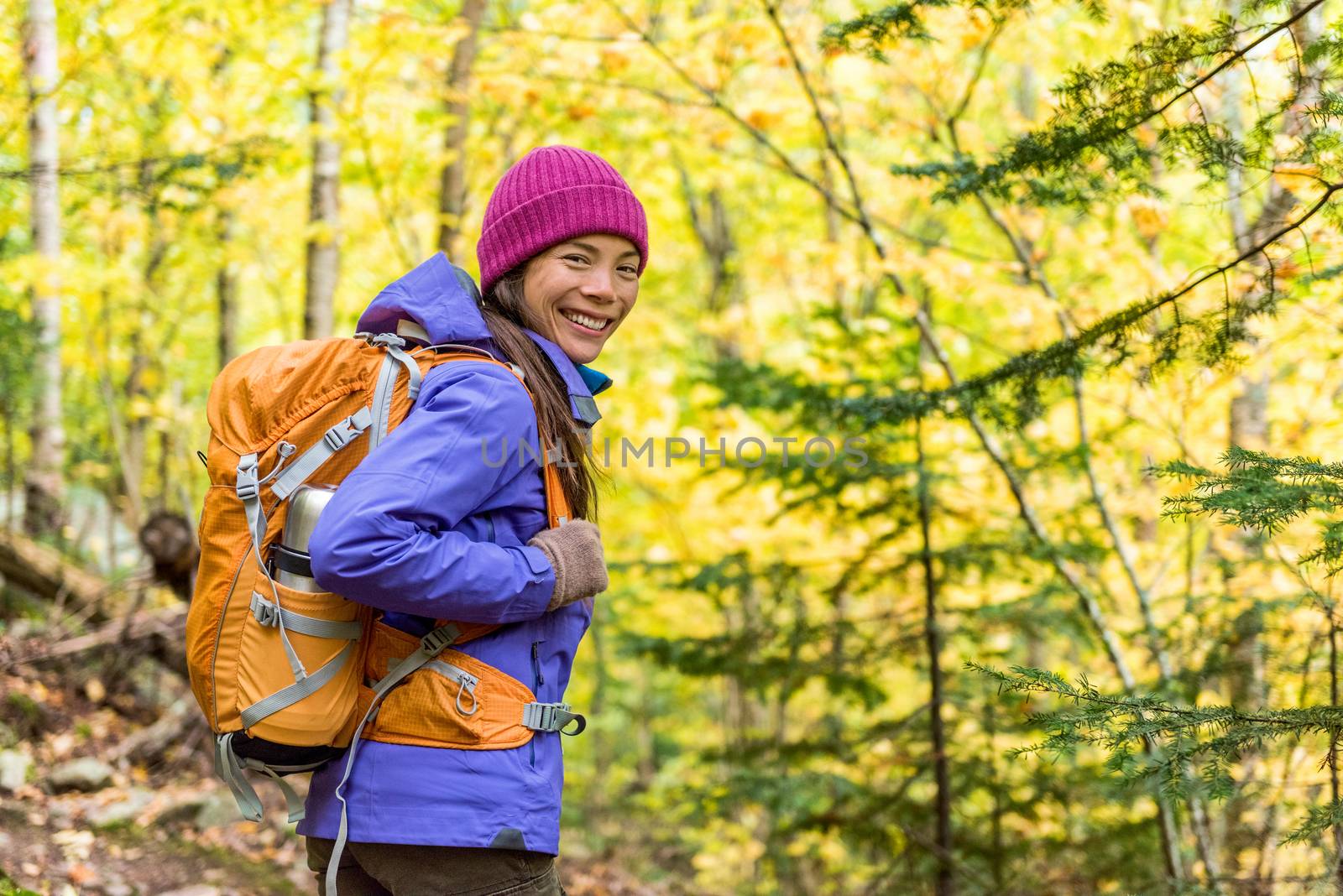 Happy backpacker girl hiking in autumn forest. Young asian hiker woman in outdoor gear for cold weather with backpack looking at camera enjoying walking in nature outdoors in fall season. by Maridav