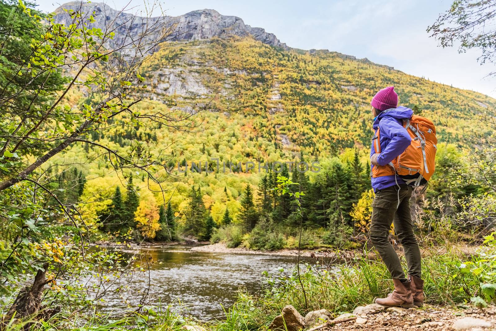 Woman hiker hiking looking at scenic view of fall foliage mountain landscape . Adventure travel outdoors person standing relaxing near river during nature hike in autumn season. by Maridav