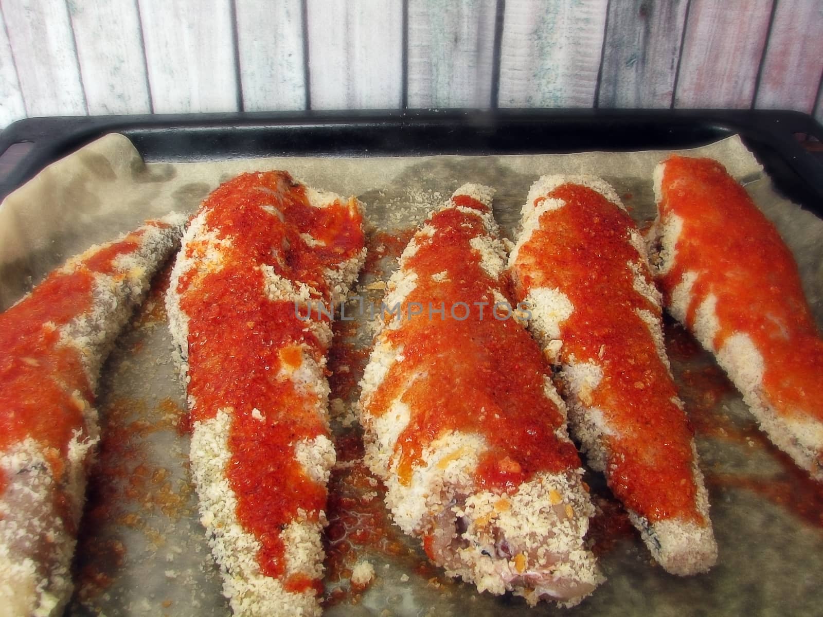 fresh sea fish breaded in breadcrumbs and prepared for baking on a baking sheet