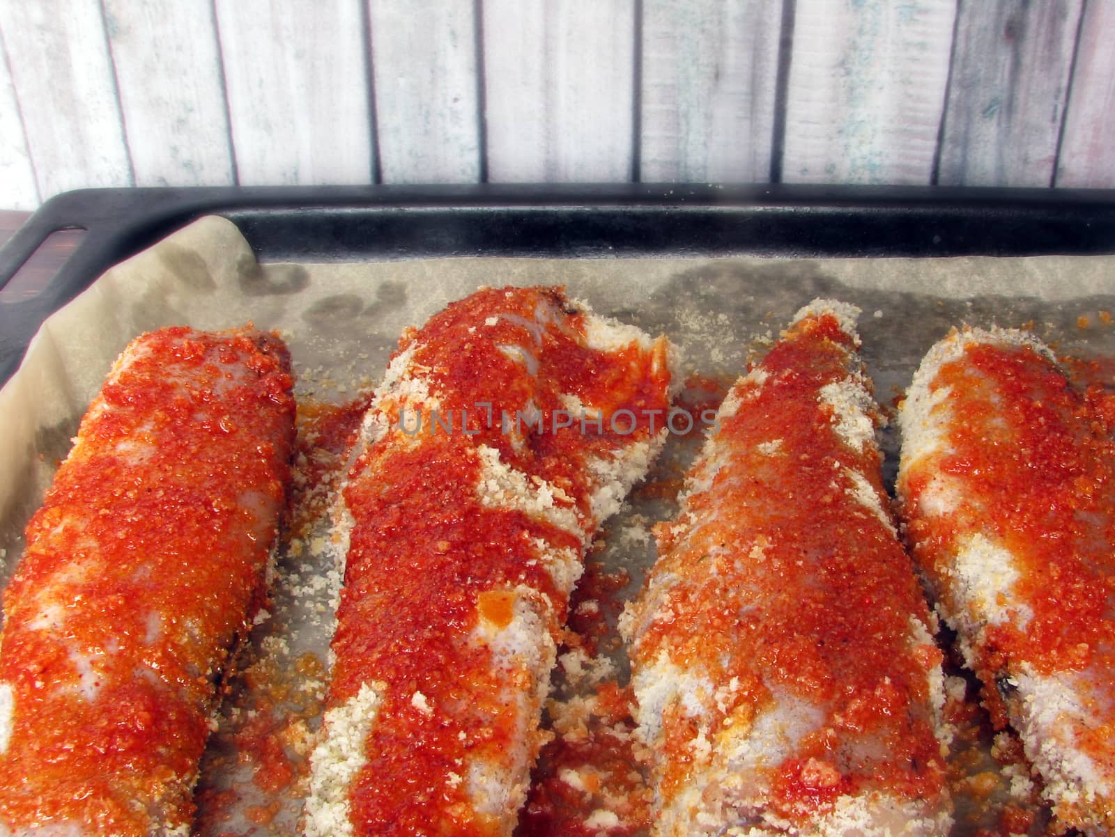 fresh sea fish breaded in breadcrumbs and prepared for baking on a baking sheet
