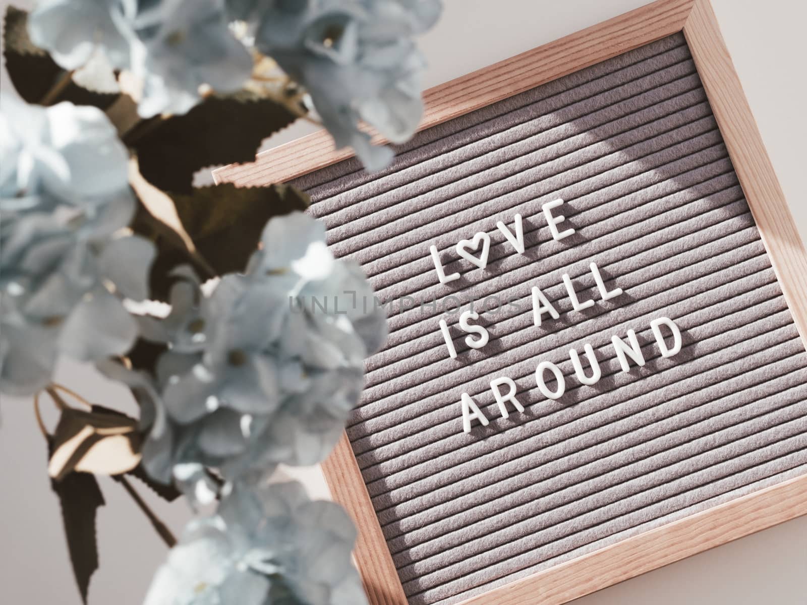 Top view on letter board with words LOVE IS ALL AROUND. Flat lay concept heart symbol of love and romance. Blue hydrangea flowers.