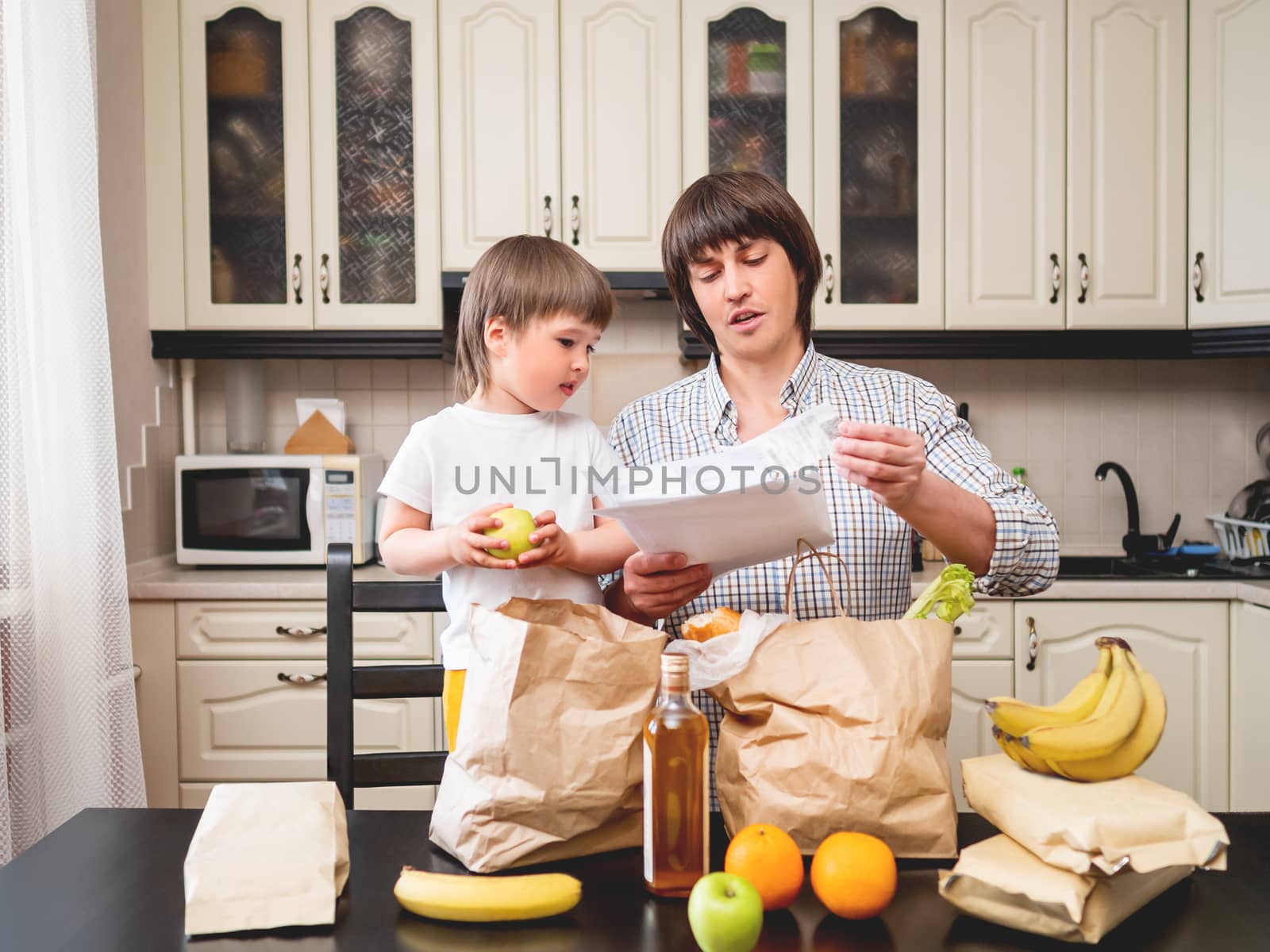Family sorts out purchases in the kitchen. Father and son tastes products in bags made of craft paper. Healthy nutrition for whole family.