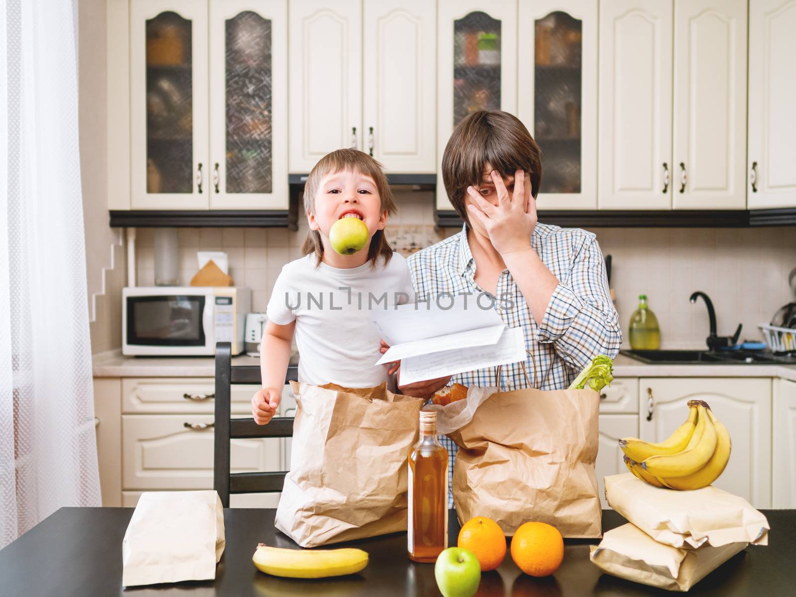 Family sorts out purchases in the kitchen. Father and son tastes products in bags made of craft paper. Expensive healthy nutrition.