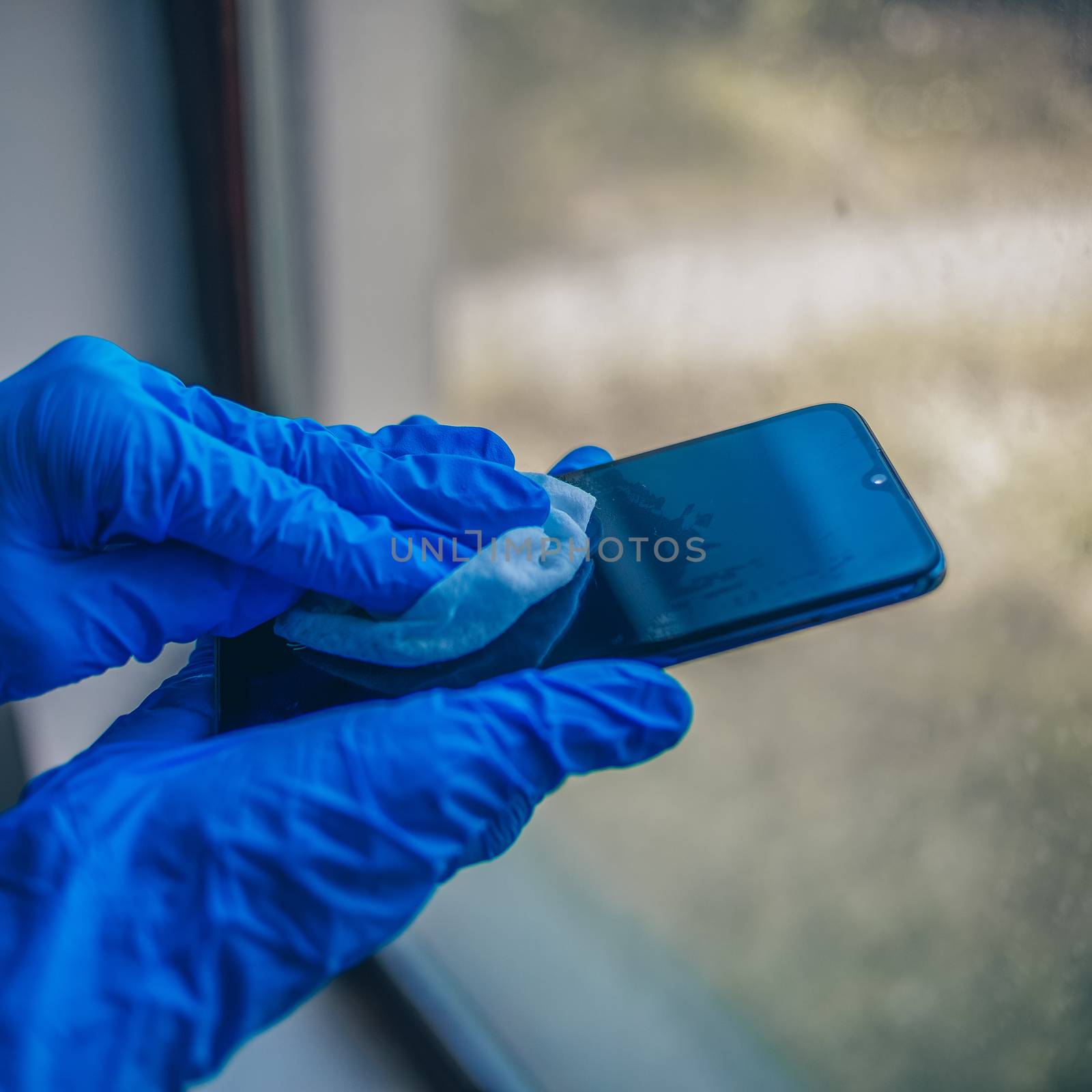 Woman's hand in blue gloves cleaning smartphone mobile phone wit by adamr