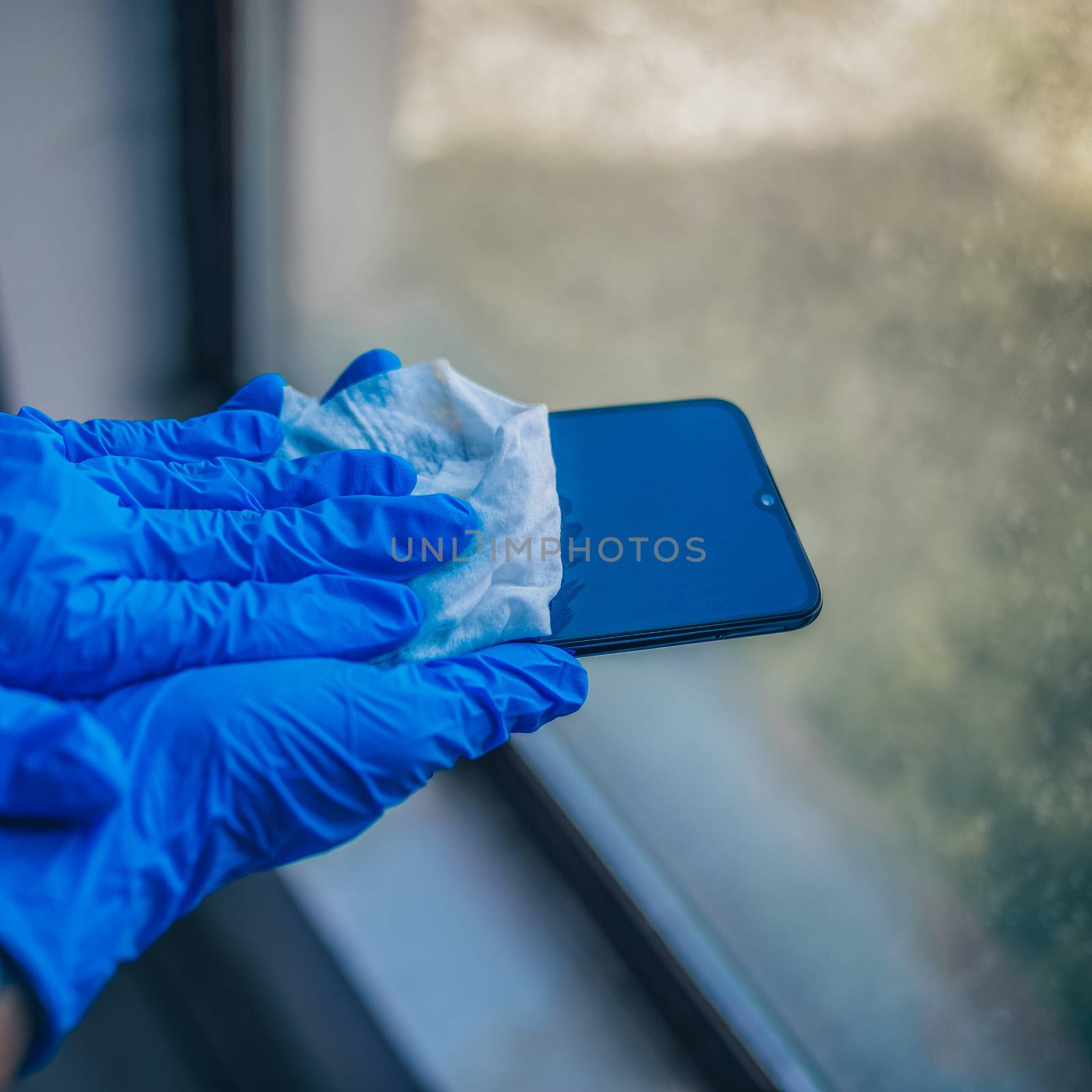 Woman's hand holding in blue gloves and sanitizing cleaning smartphone mobile phone with wet wipes