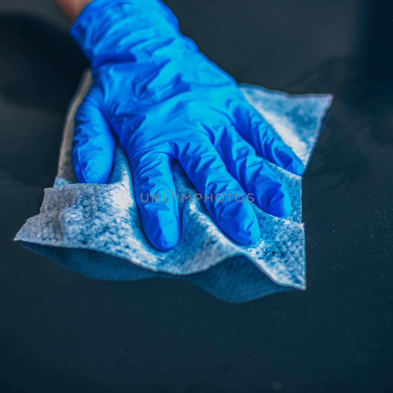 Woman's hand in blue gloves cleaning home office table surface with wet wipes