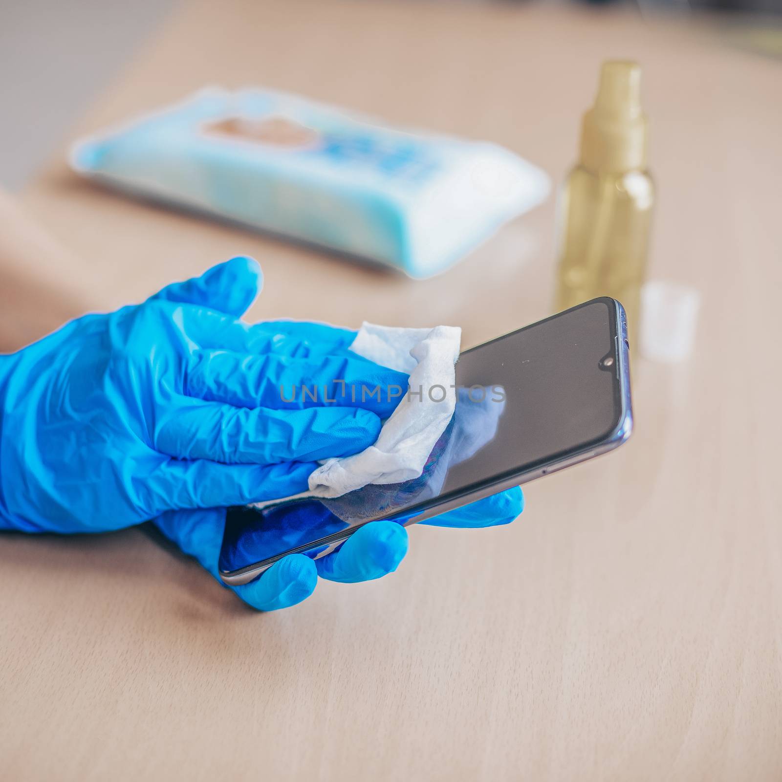 Woman's hand in blue gloves sanitizing cleaning smartphone mobil by adamr
