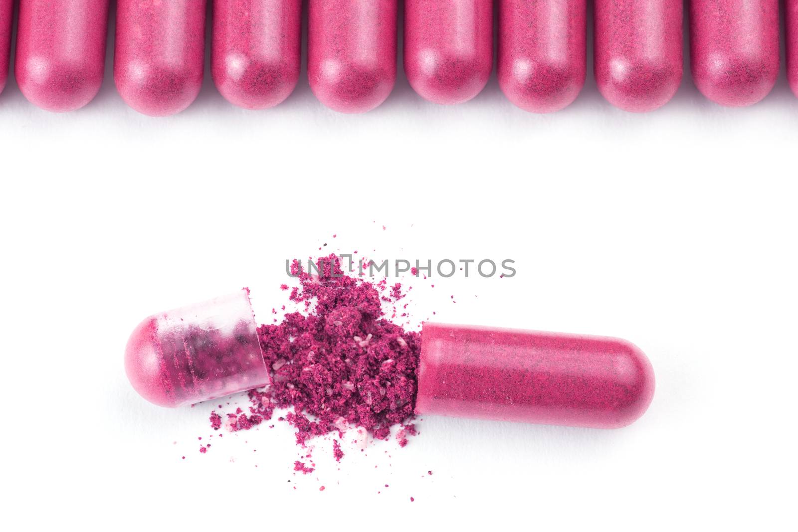 row of plastic pink color organic capsules isolated on white background closeup with one opened.
