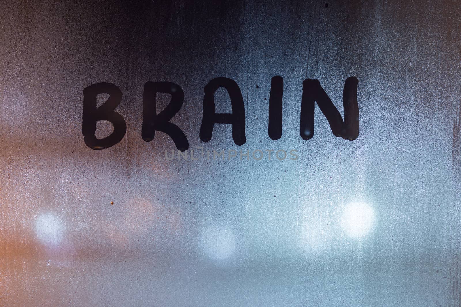 the word brain written on night wet window glass close-up with blurred background.