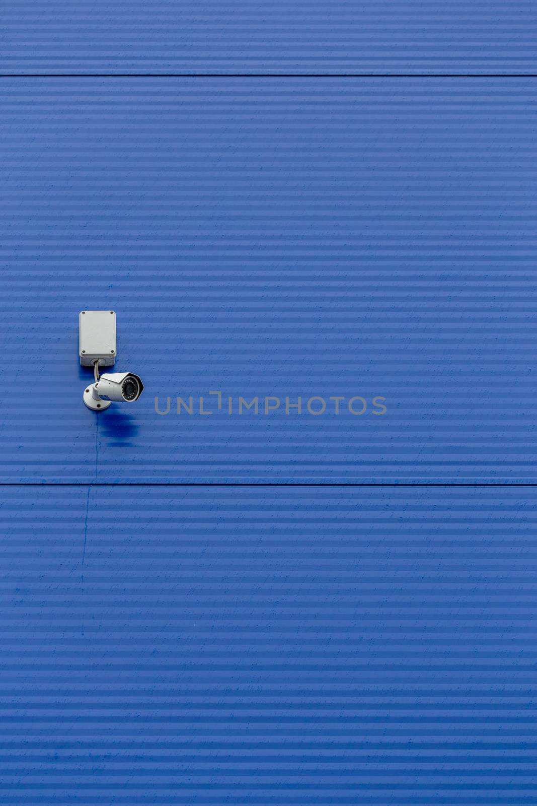 small white security camera on large blue steel silo wall.