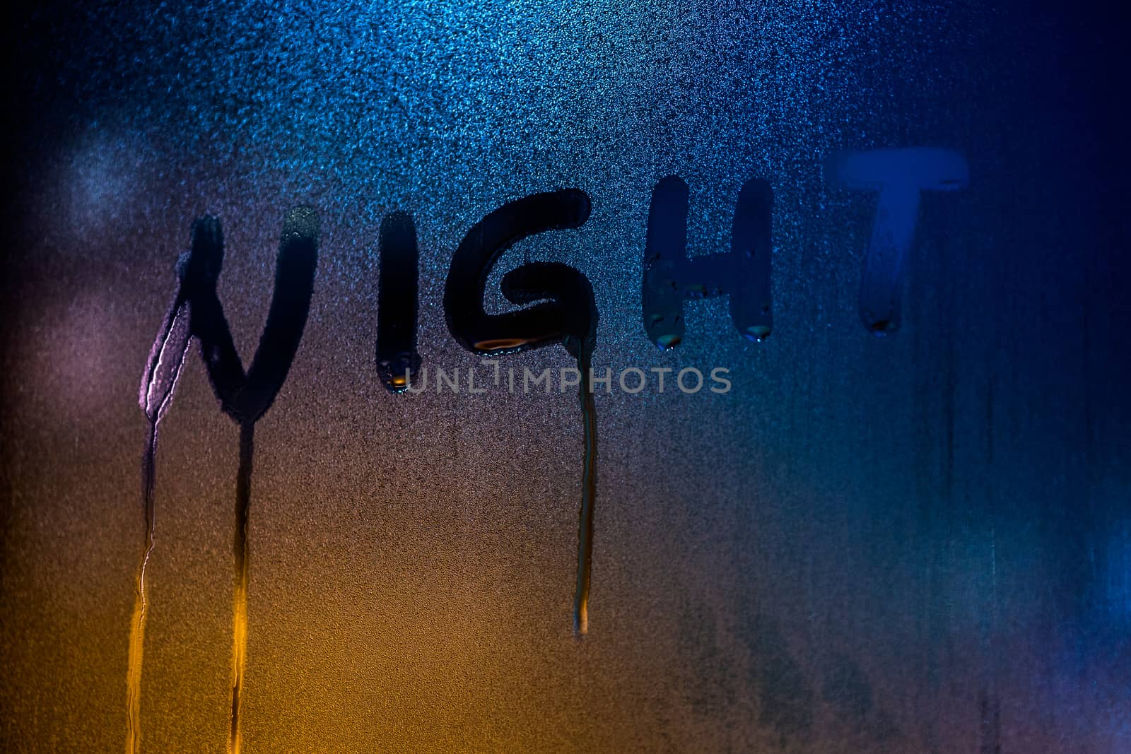 the word NIGHT written on nightime wet window glass close-up with blurred background.