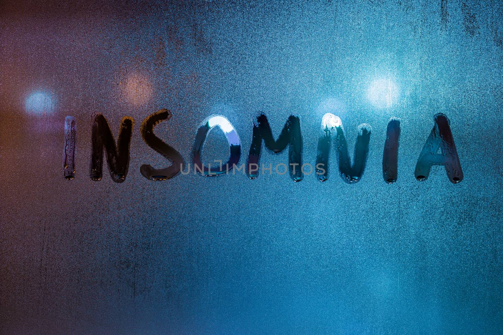 the word insomnia written on night wet window glass close-up with blurred background.