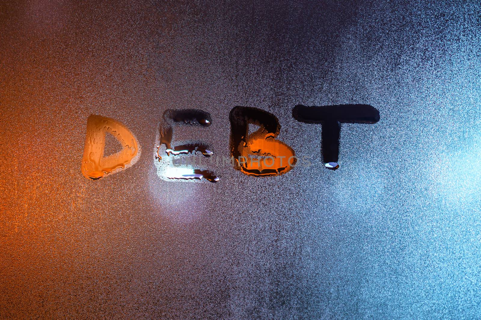 the word debt handwritten on night wet window glass close-up with blurred background.