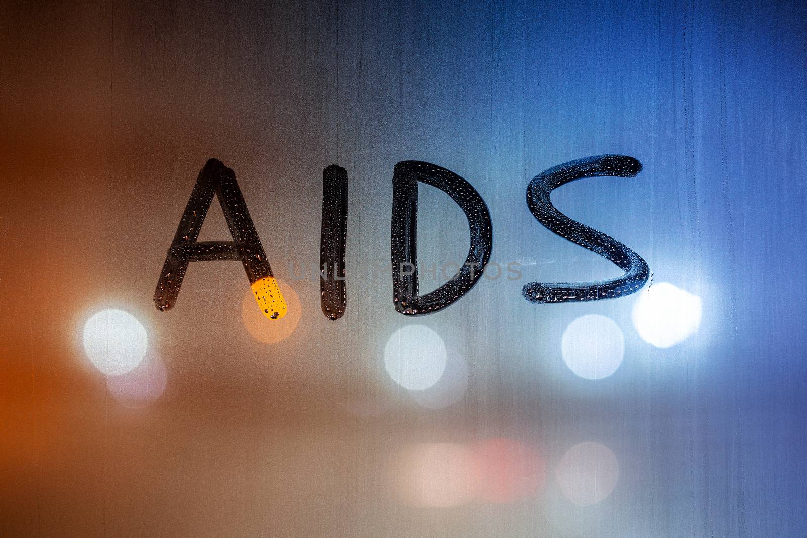the word AIDS written on night wet window glass close-up with bokeh background.