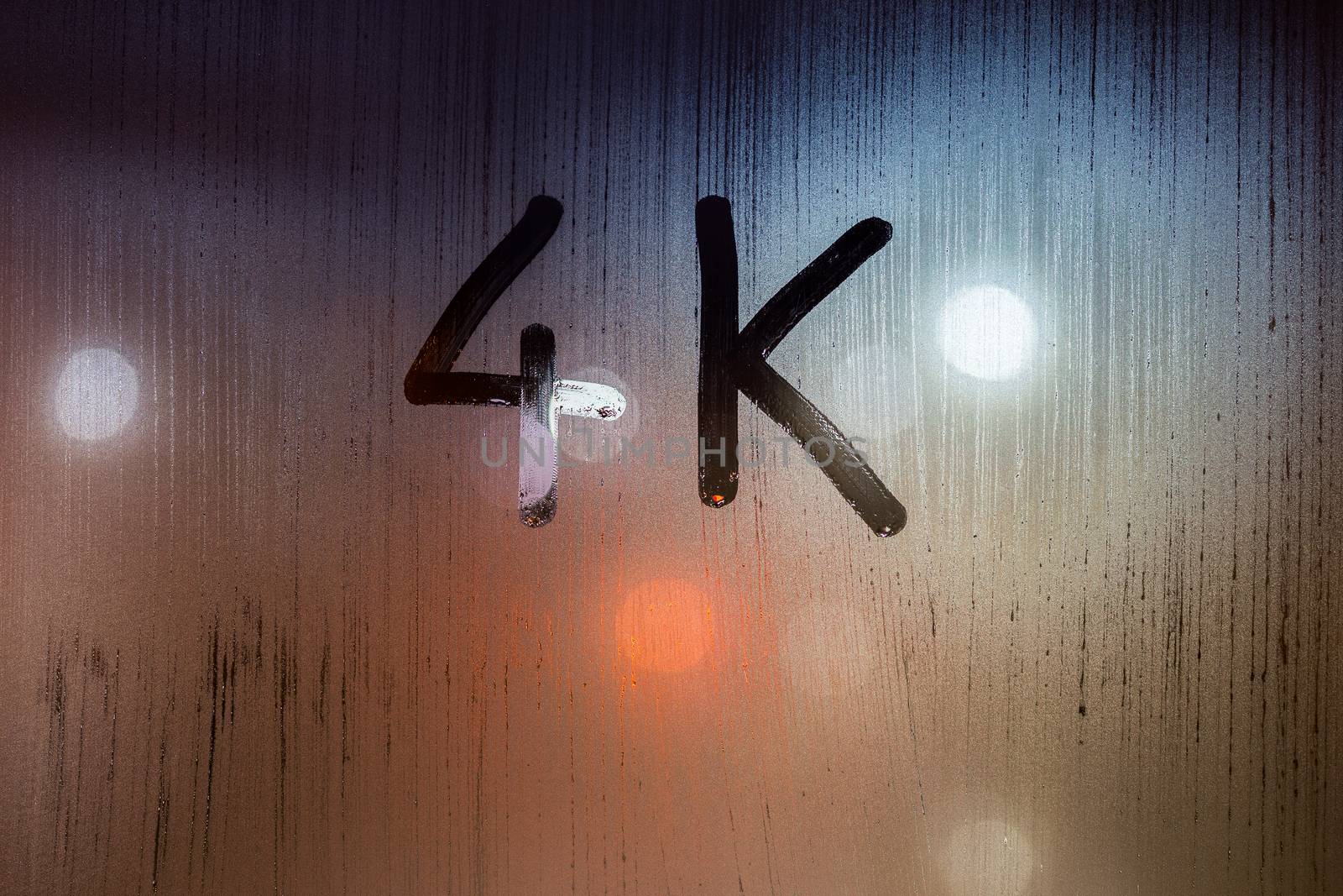 a handwritten word 4k on wet glass with blurred night lights in background.