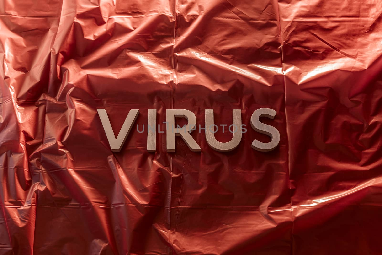 the word virus laid with brushed silver metal letters on red background of crumpled plastic film in horizontal centered composition and dramatic light