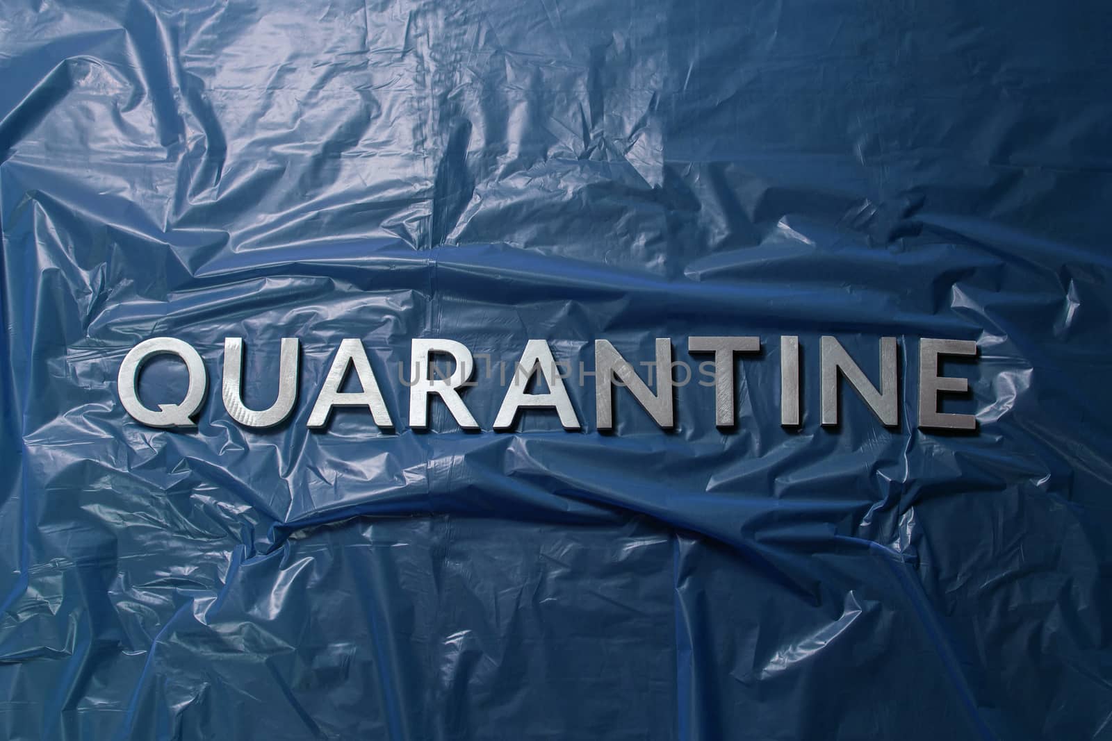 the word quarantine laid with silver letters on crumpled blue plastic film in flat lay centered composition and dramatic light