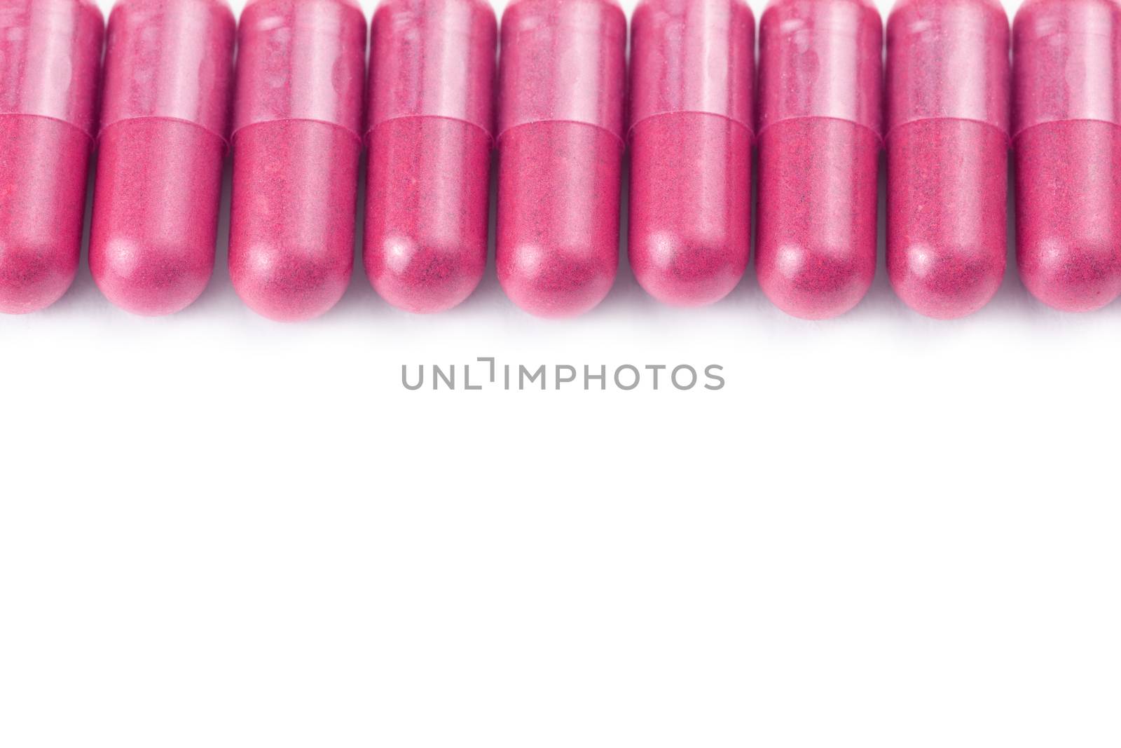 row of plastic pink color organic capsules isolated on white background closeup with selective focus.