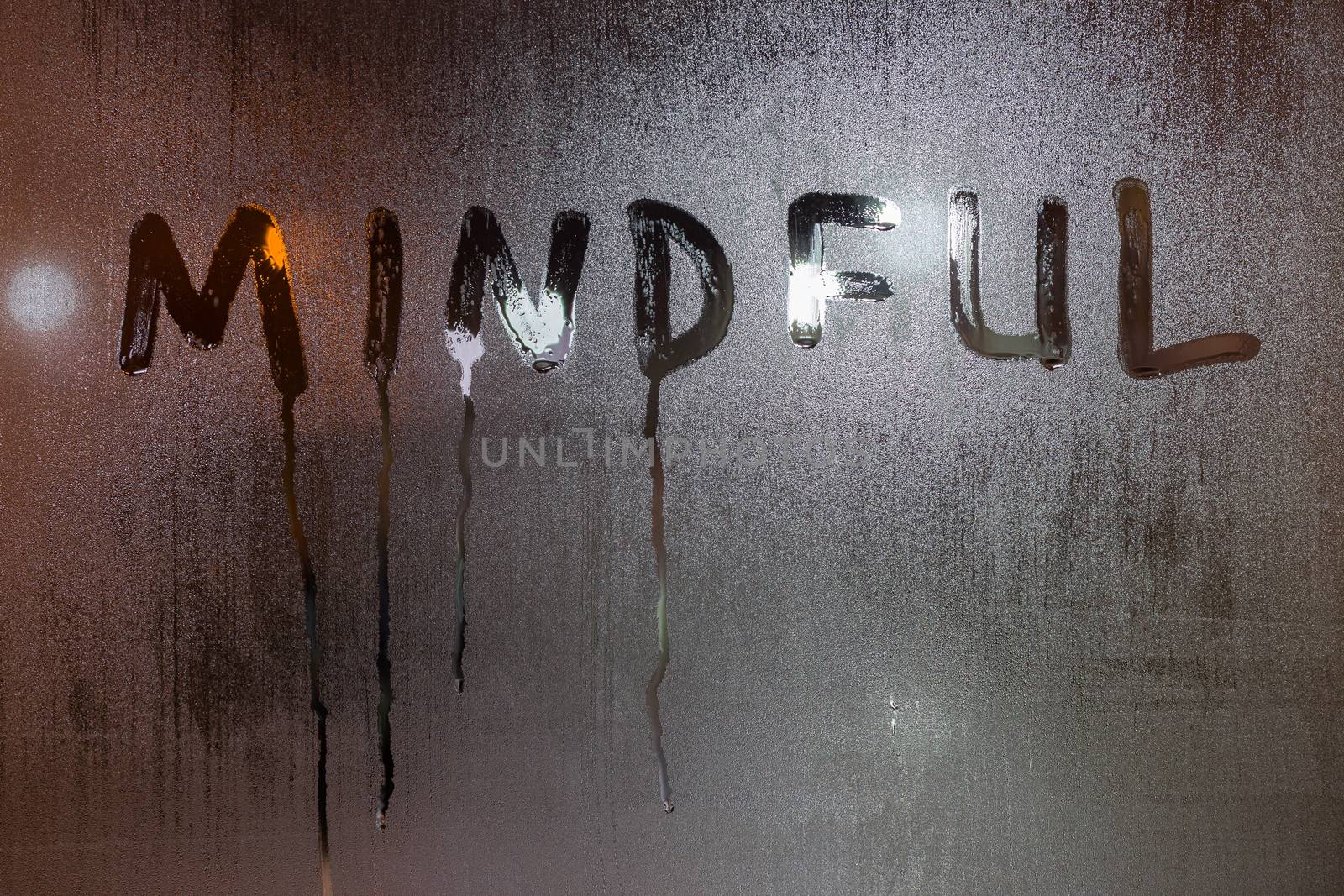 the word mindful written on night wet window glass close-up with blurred background.
