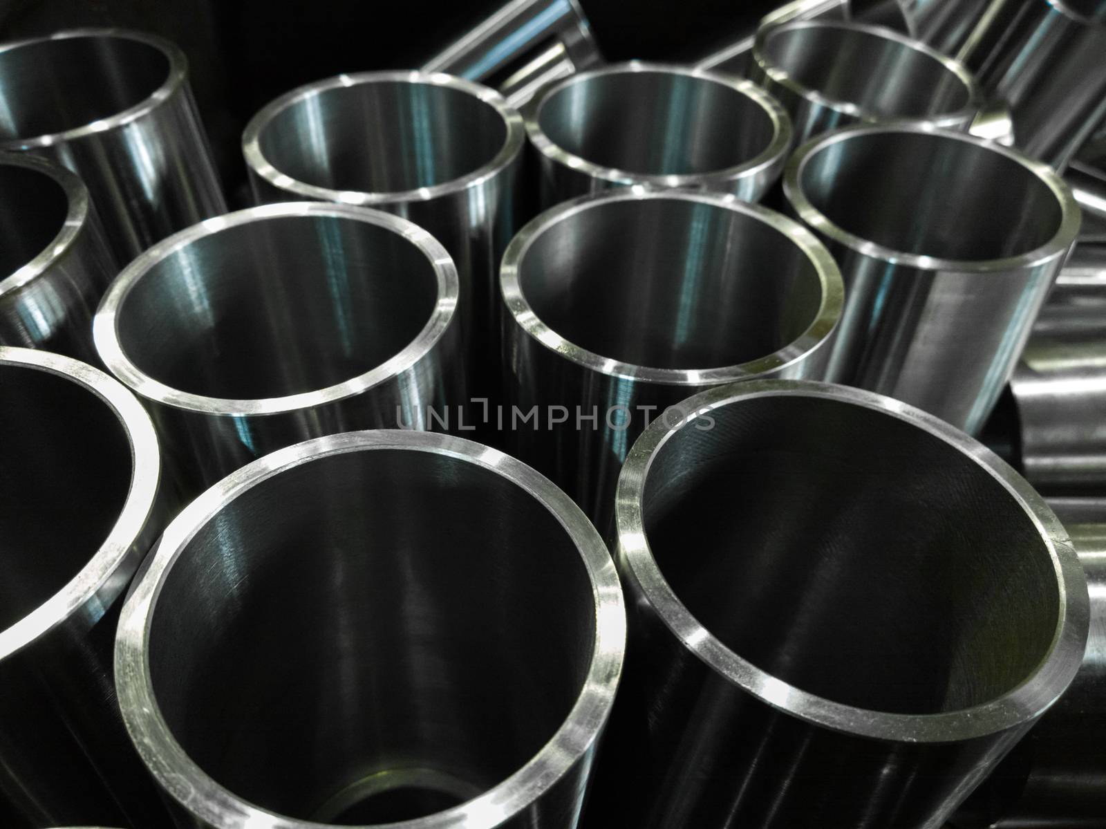 dark industrial background with cnc machined shiny steel pipes - selective focus and lens blur technique