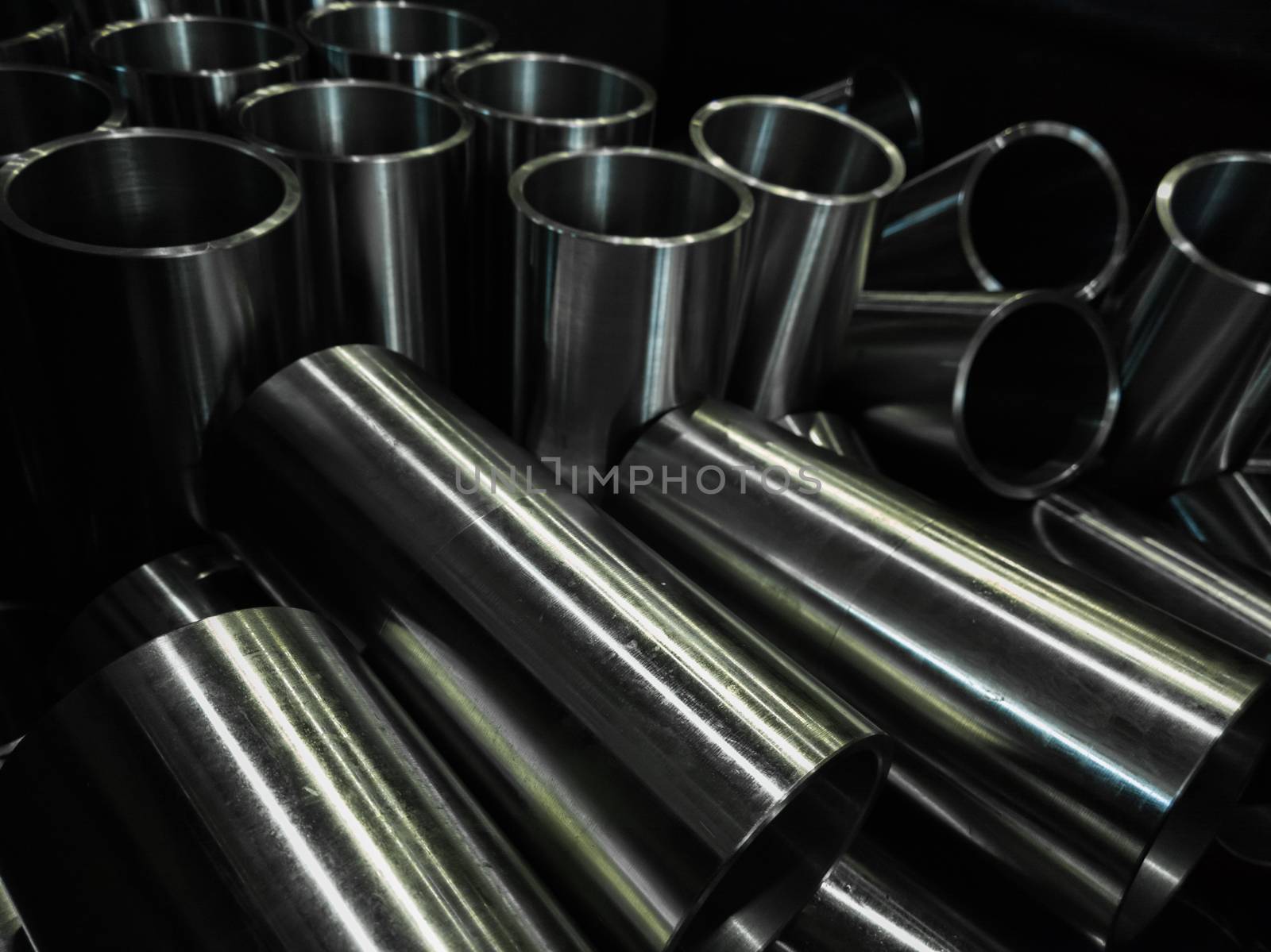 dark industrial background with cnc machined shiny steel pipes - selective focus and lens blur technique
