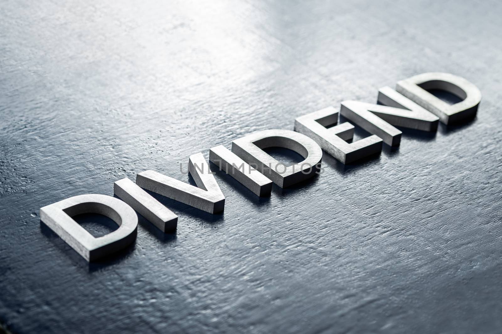 the word dividend laid by silver metal letters on gloss painted board background with selective focus in diagonal perspective