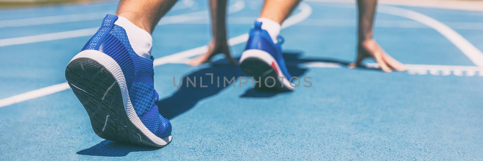 Sprinter waiting for start of race on running tracks at outdoor stadium. Sport and fitness runner man athlete on blue run track with running shoes. Banner panorama. by Maridav