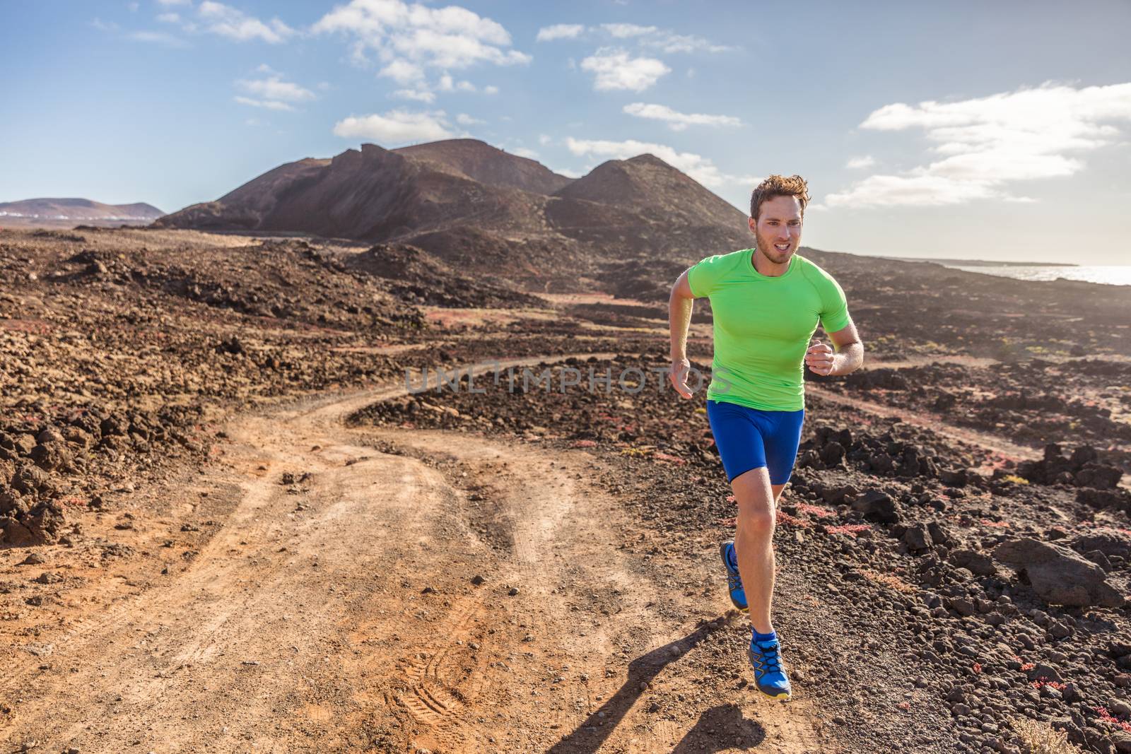 Trail runner male athlete running in nature rocky volcanic mountain background. Active fit sports man in compression sportswear sprinting on rocks path working out cardio training body.
