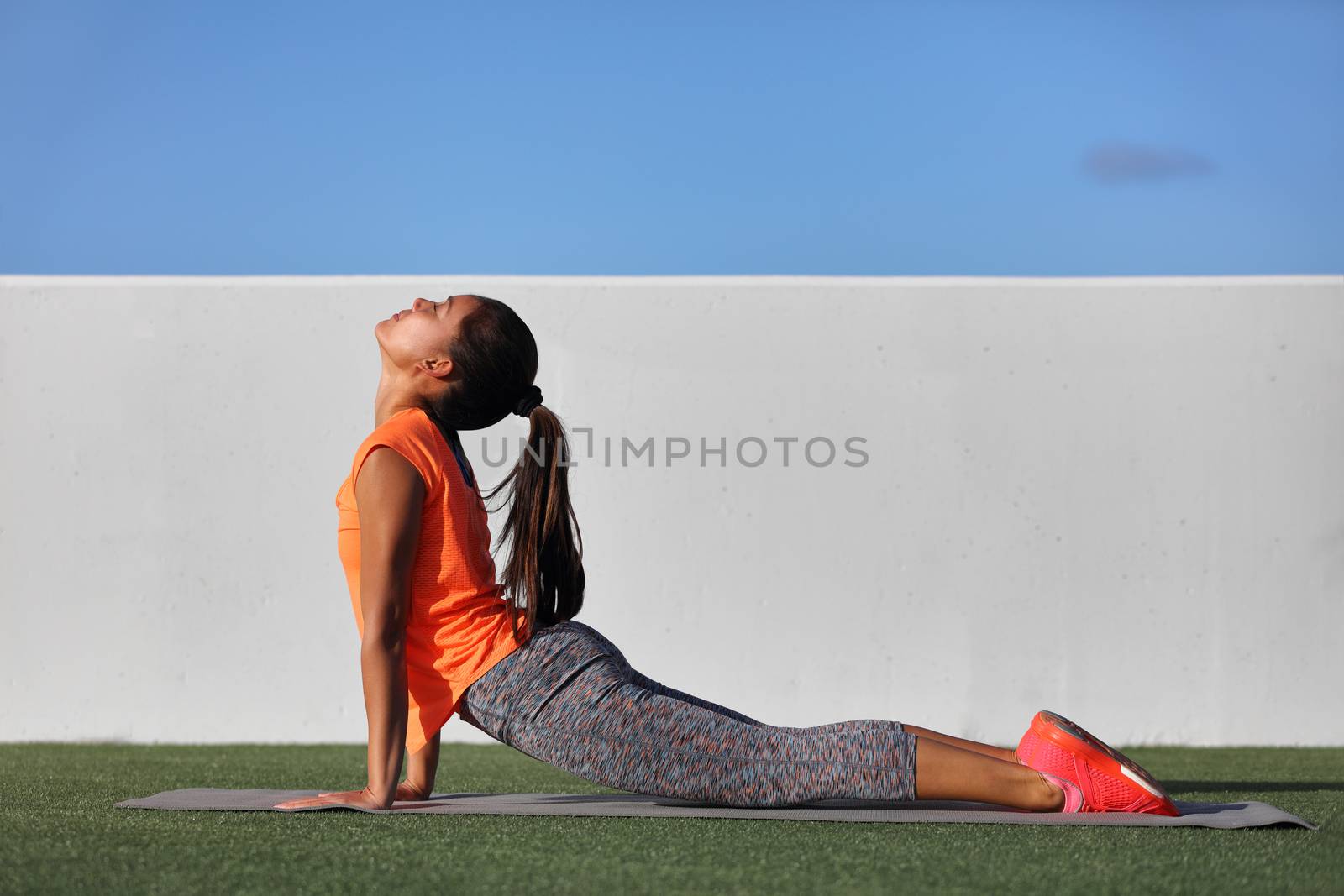 Fitness yoga woman stretching practicing morning sequence doing cobra pose or upward facing dog, bhujangasana. Fit fitness girl stretching summer park grass. Beautiful multiracial female model.
