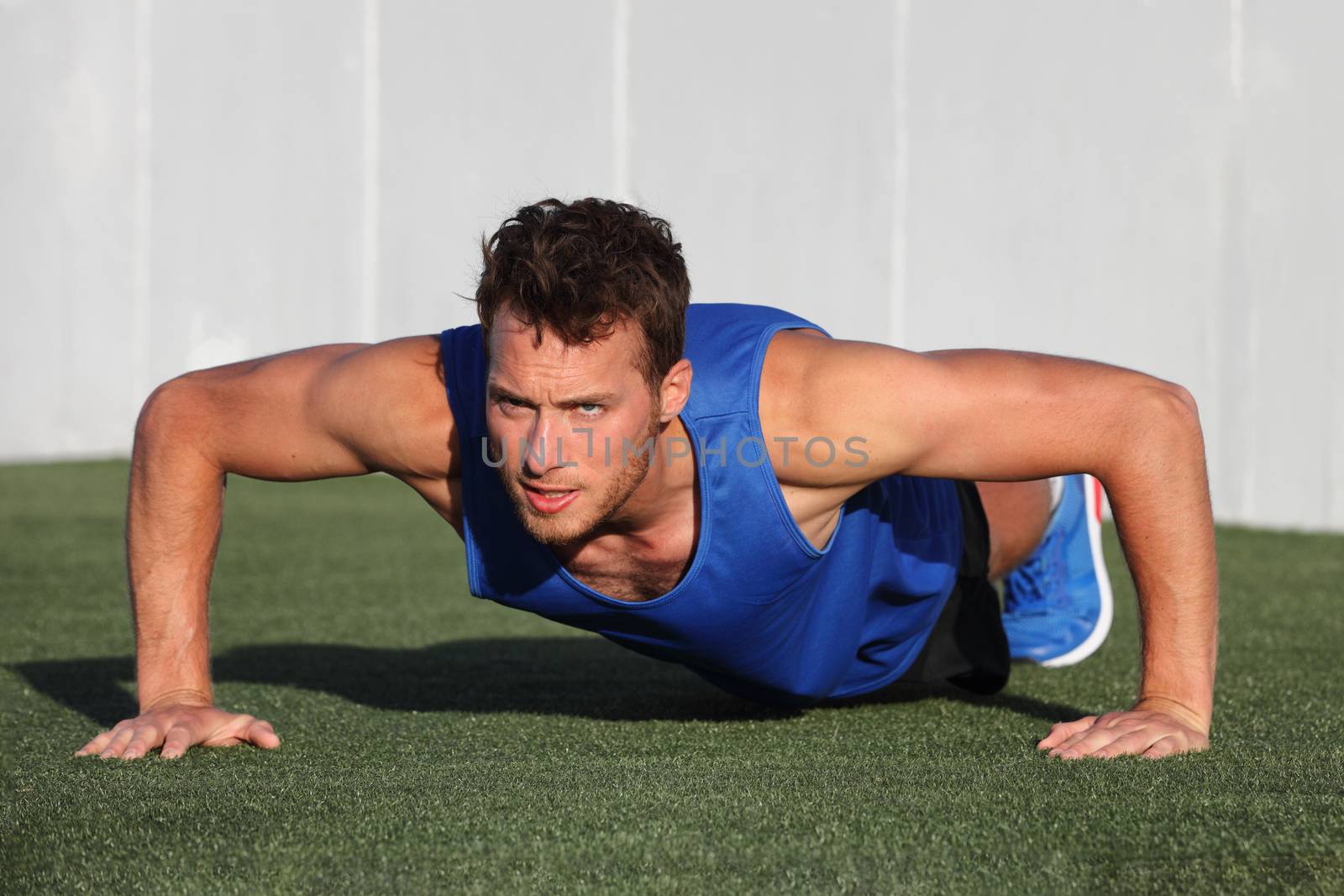 Push ups - fitness man exercising outside doing pushups. Male fitness instructor doing Push Ups on stadium grass at outdoor gym center.
