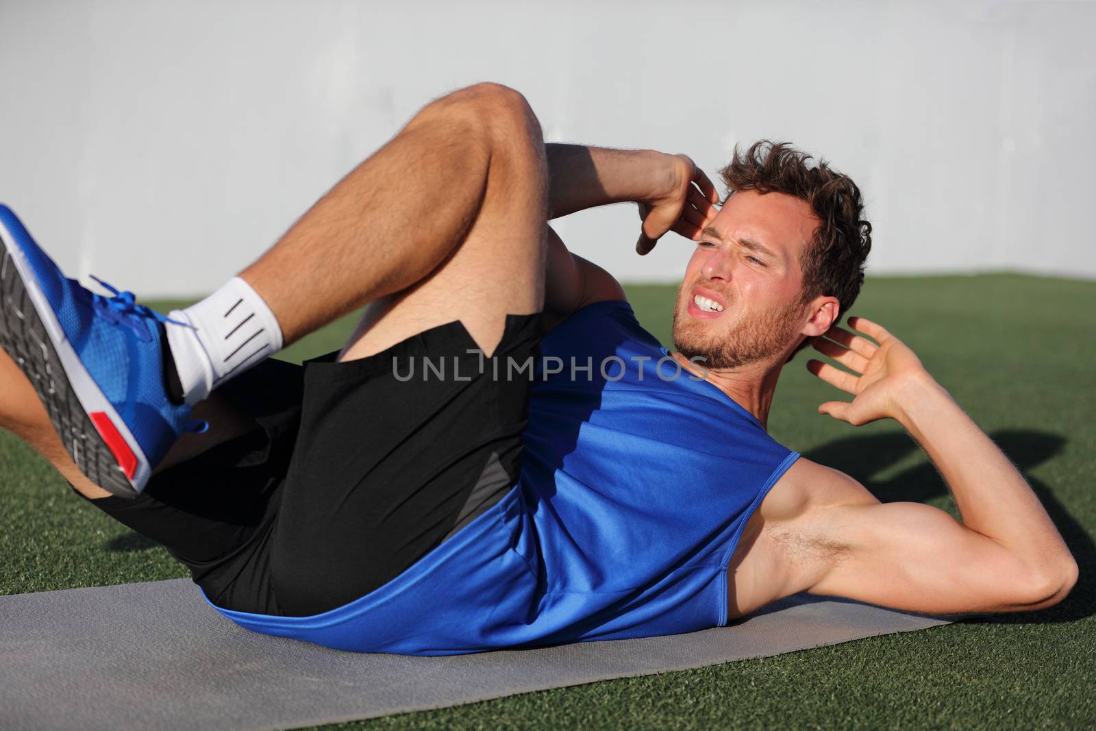 Sit ups - fitness man exercising oblique abs workout with bicycle situps outside in grass in summer. Fit male athlete working out cross training in summer. Caucasian muscular sports model in his 20s.