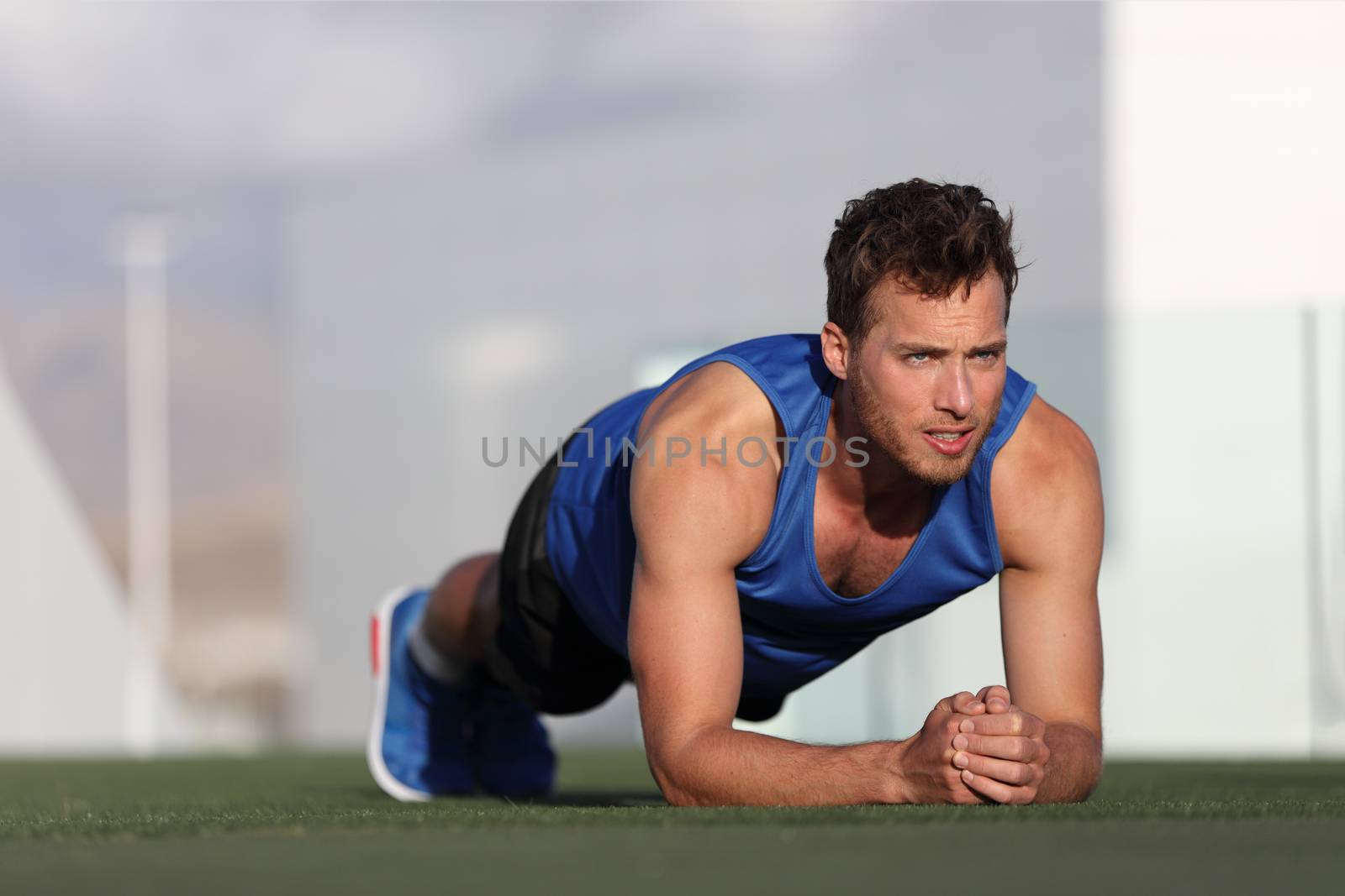 Crossfit training fitness man doing plank core exercise working out his midsection core muscles. Fit male fitness instructor planking exercising outside in summer park grass. Outdoor stadium. by Maridav