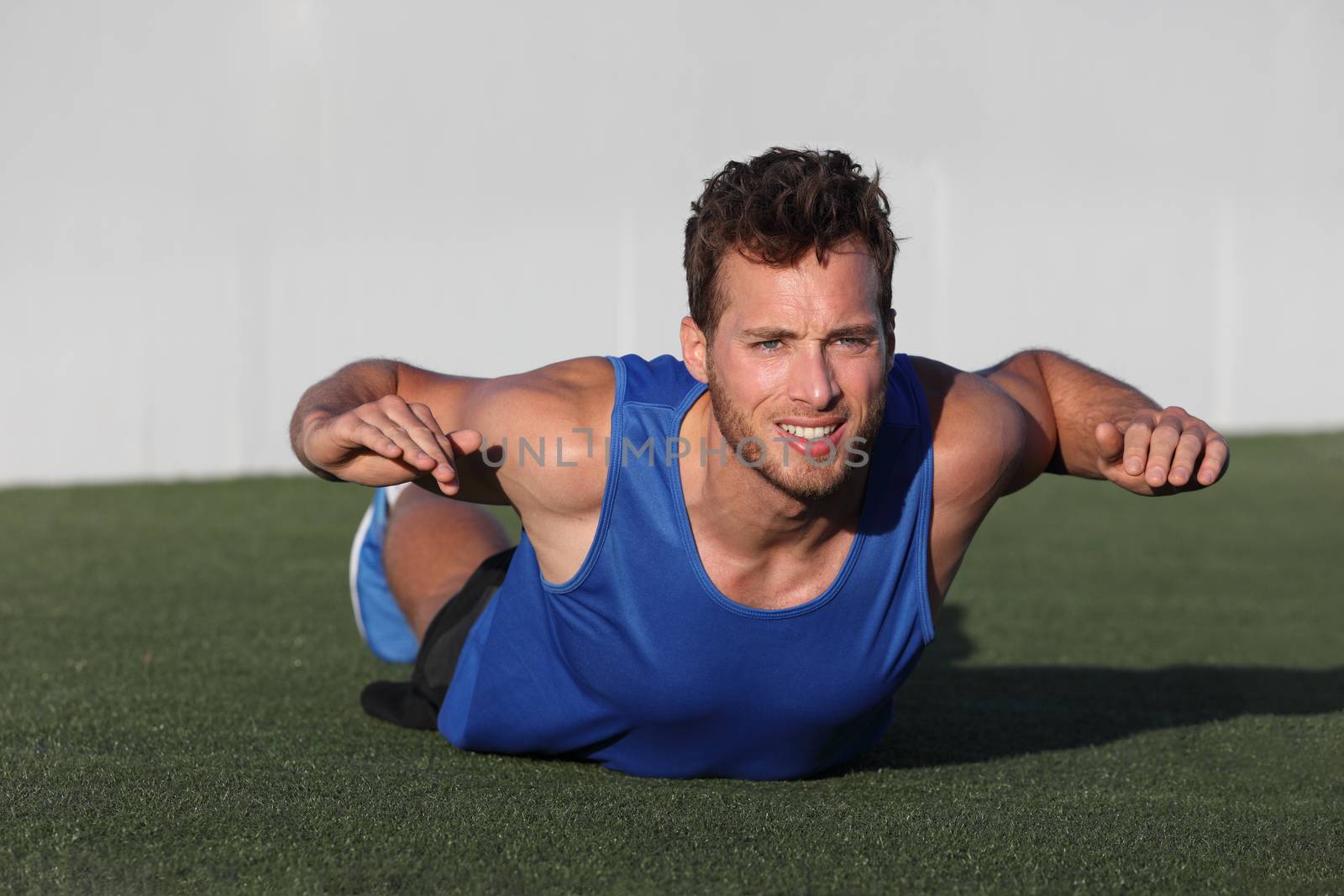 Fitness training back fat exercise fit man doing superman variation of lower body workout. Strong athlete working out outdoors in park grass. Lower body back lumbar muscles strengthening exercises.