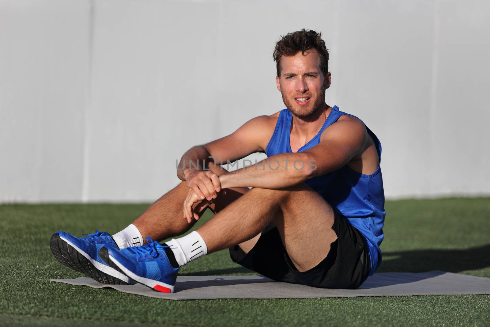 Gym fitness man portrait relaxing on exercise mat at outdoor park . Happy fit male athlete healthy active lifestyle ready for morning yoga practice at home outside on grass.