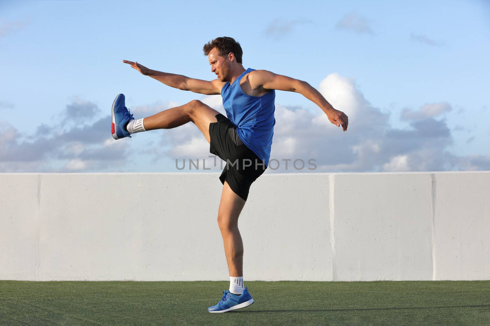 Runner man getting ready to run doing warm-up dynamic leg stretch exercises routine, Male athlete stretching lower body hamstring muscles before going running outside in summer outdoors. by Maridav