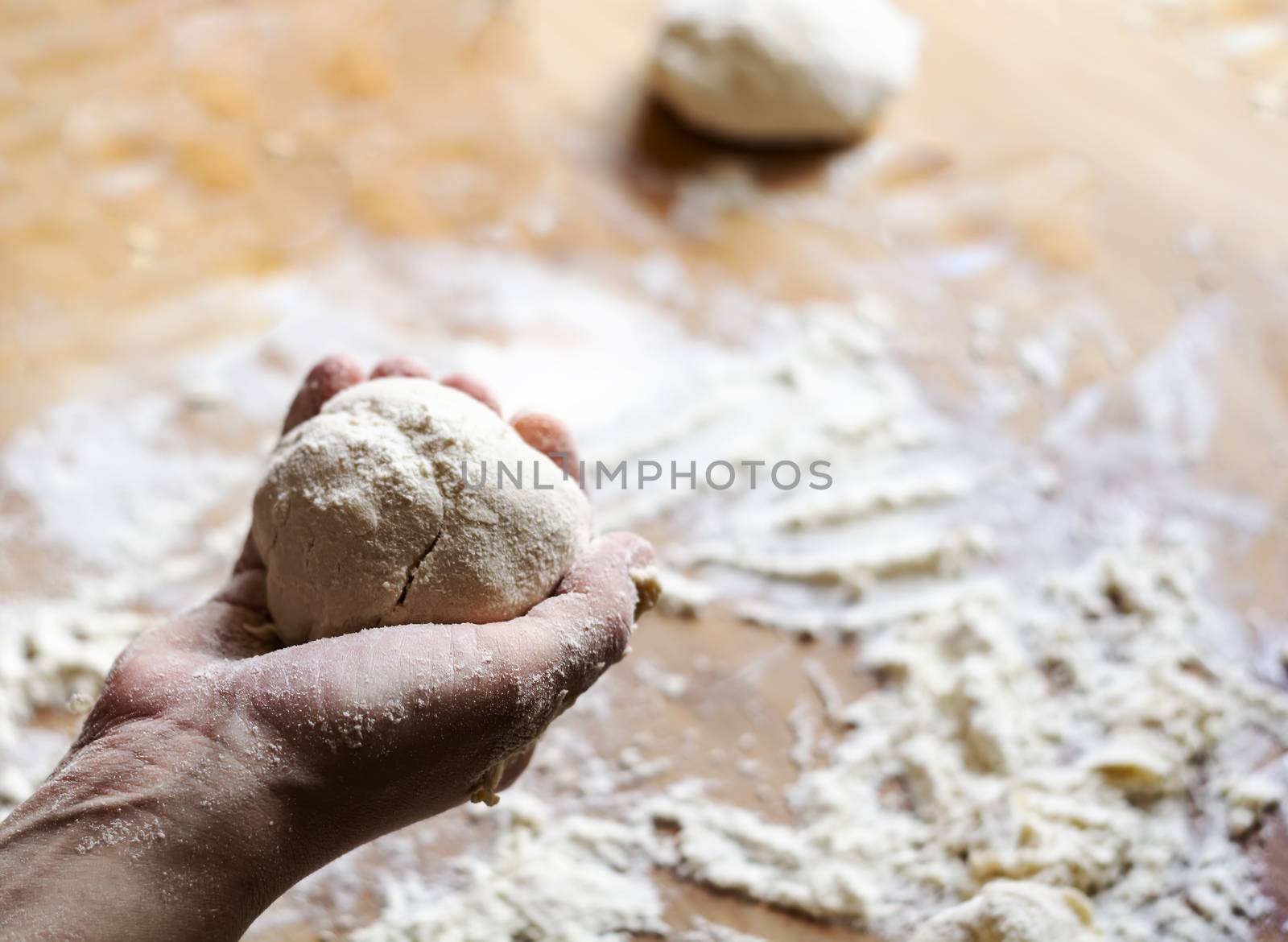 a female hand holds a flour dough with a wooden board dirty with flour in the background. by rarrarorro