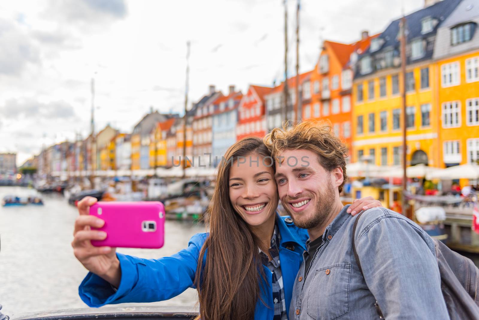 Copenhagen travel couple tourists taking selfie photo with phone camera. Smiling young people students at old port Nyhavn, tourism danish landmark in Denmark, northern Europe. by Maridav