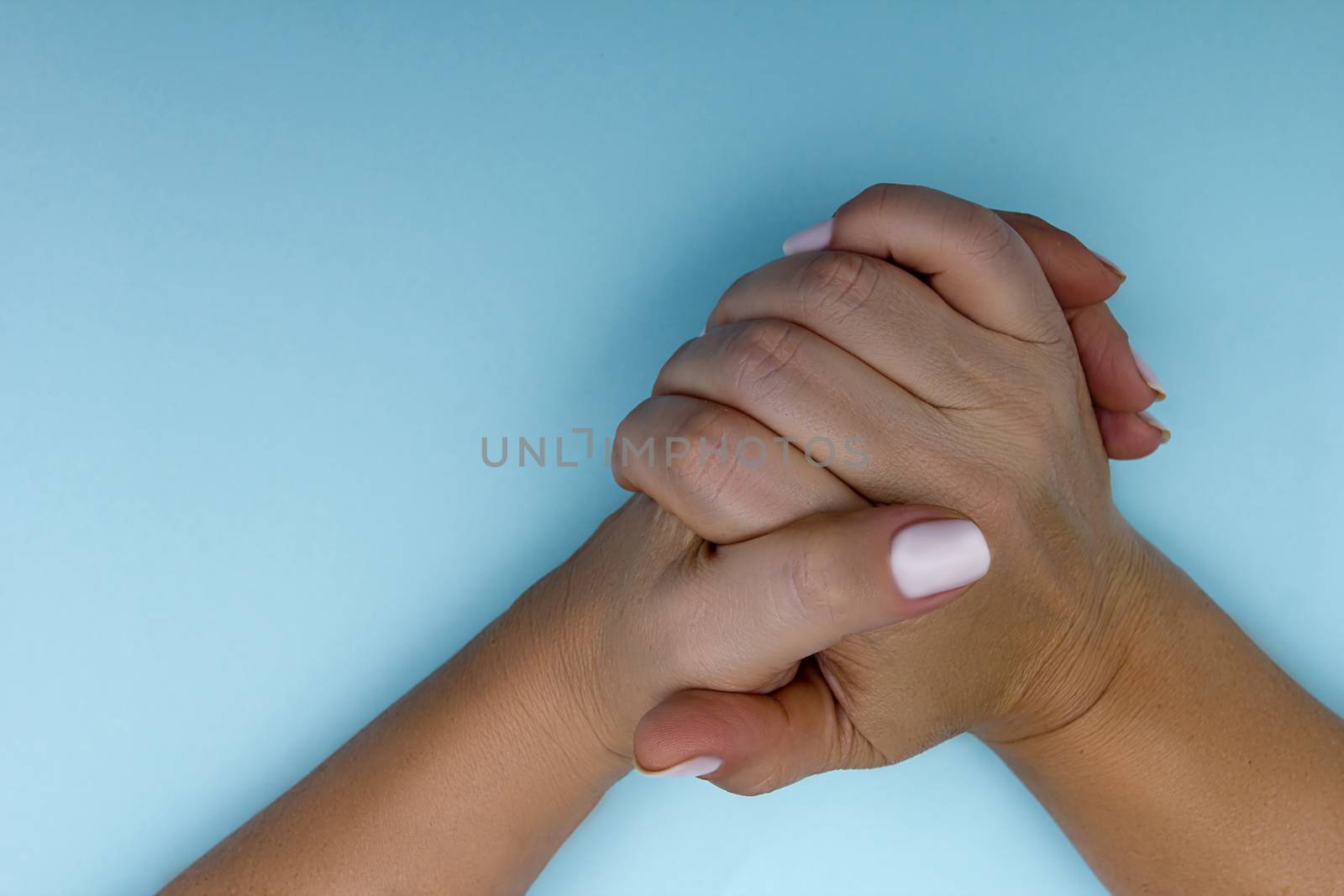 Folded female hands on a blue background