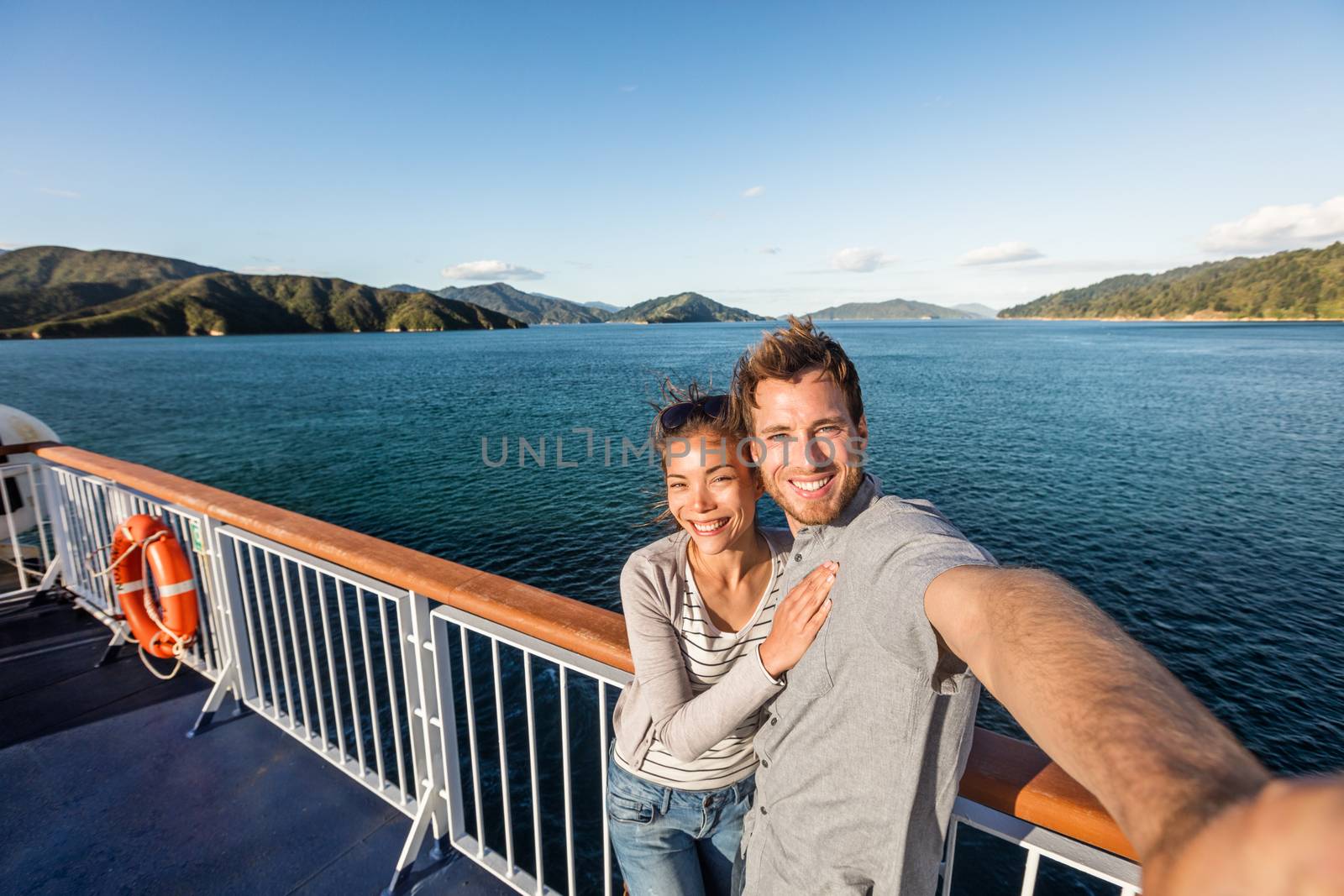 Cruise couple tourists taking selfie on New Zealand travel. People traveling on ferry boat Marlborough sounds taking self-portrait picture with mobile phone smiling at camera. by Maridav