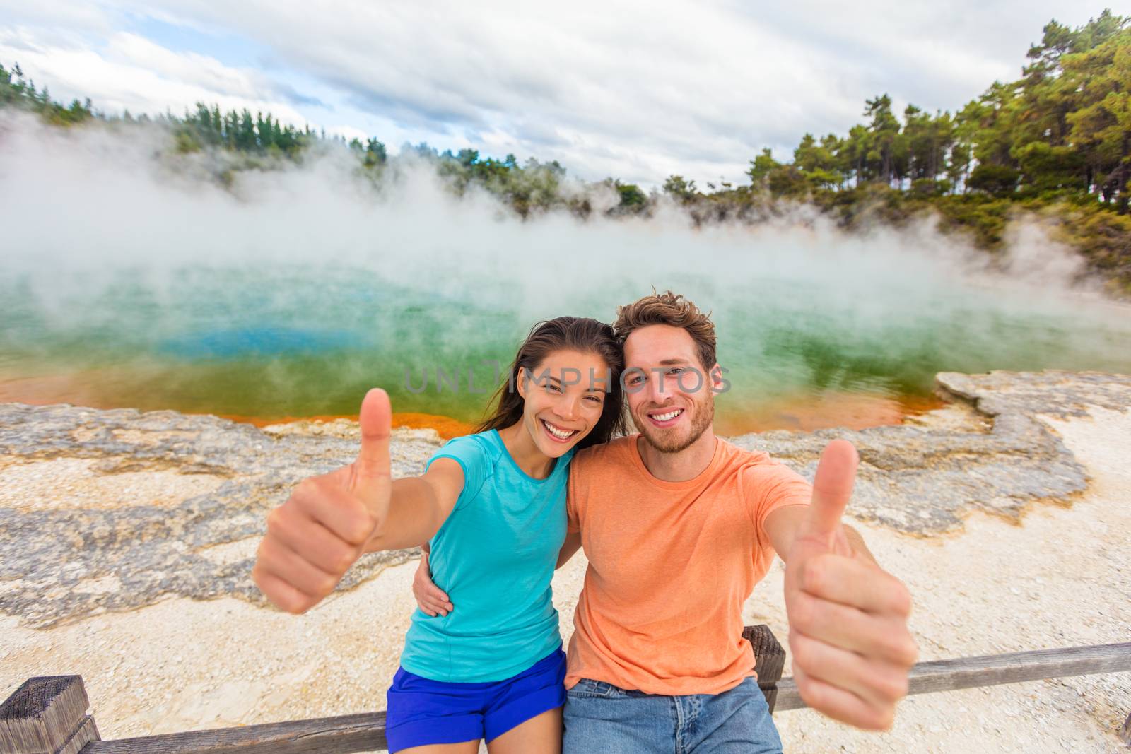 New Zealand happy tourist couple doing thumbs up at famous attraction travel destination. Champagne pool, Waiotapu. Active geothermal area, in Taupo Volcanic Zone, Rotorua, north island. by Maridav