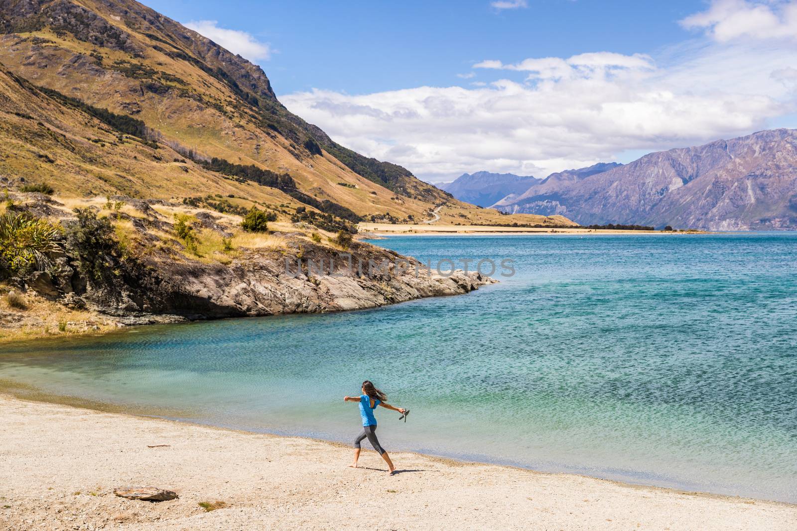 New Zealand travel happy tourist woman running of joy and freedom at beach shore of lake Hawea nature landscape. Near Wanaka, Otago Region