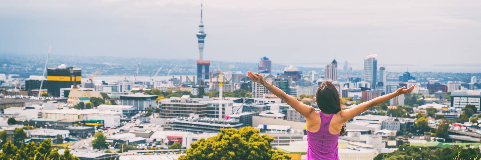 Auckland city skyline view from Mount Eden banner. Sky tower, New Zealand. Happy woman with arms up in freedom and happiness at top of Mt Eden urban park famous tourist attraction. by Maridav