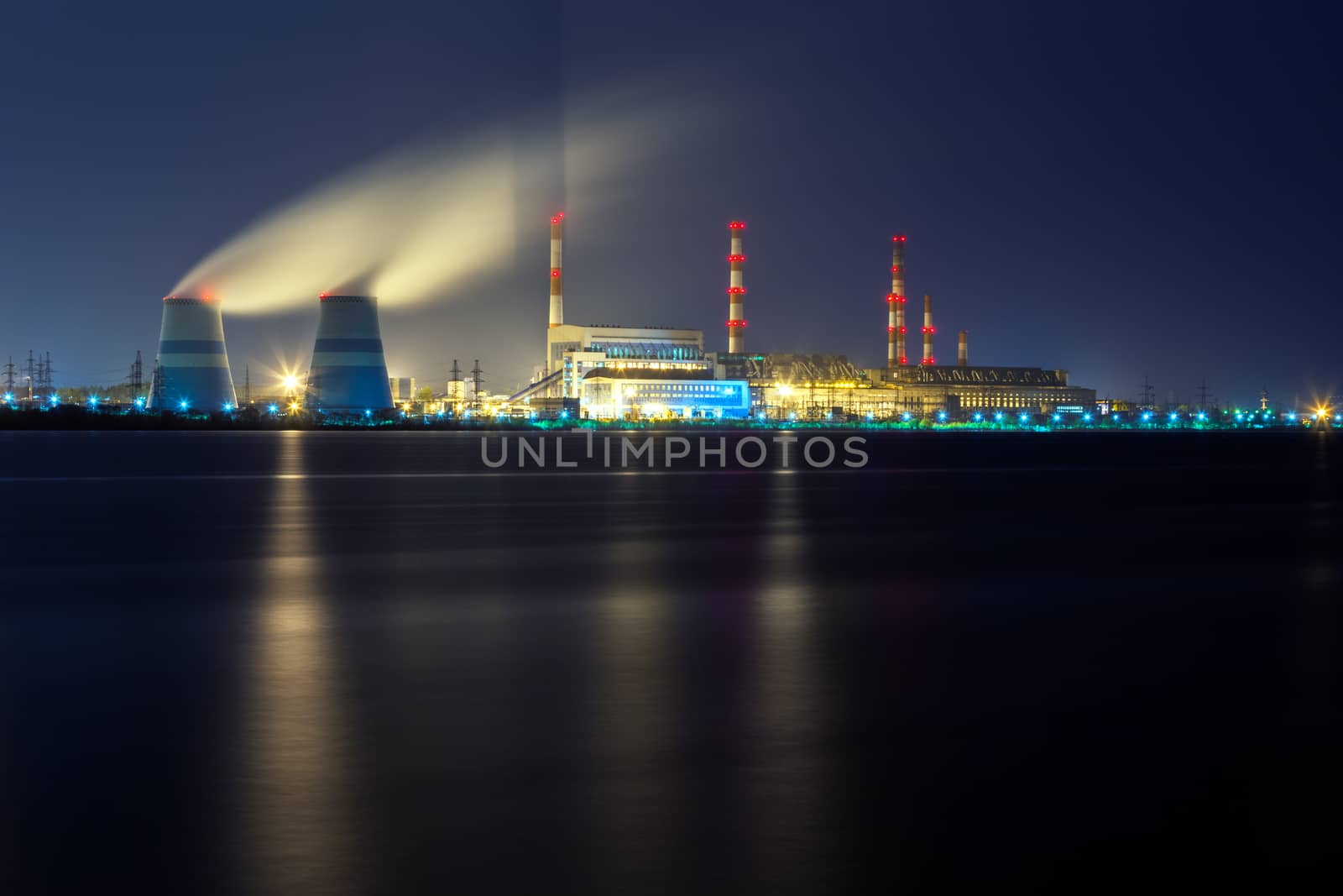 old thermal 450 megawatt power plant at night with artificial lake on foreground.