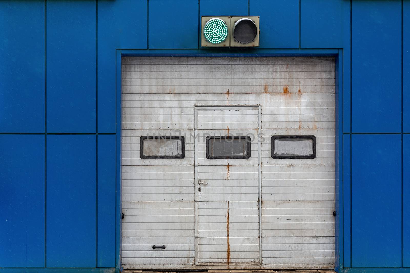 a white automatic upward sliding gate on blue garage with green lit traffic light.