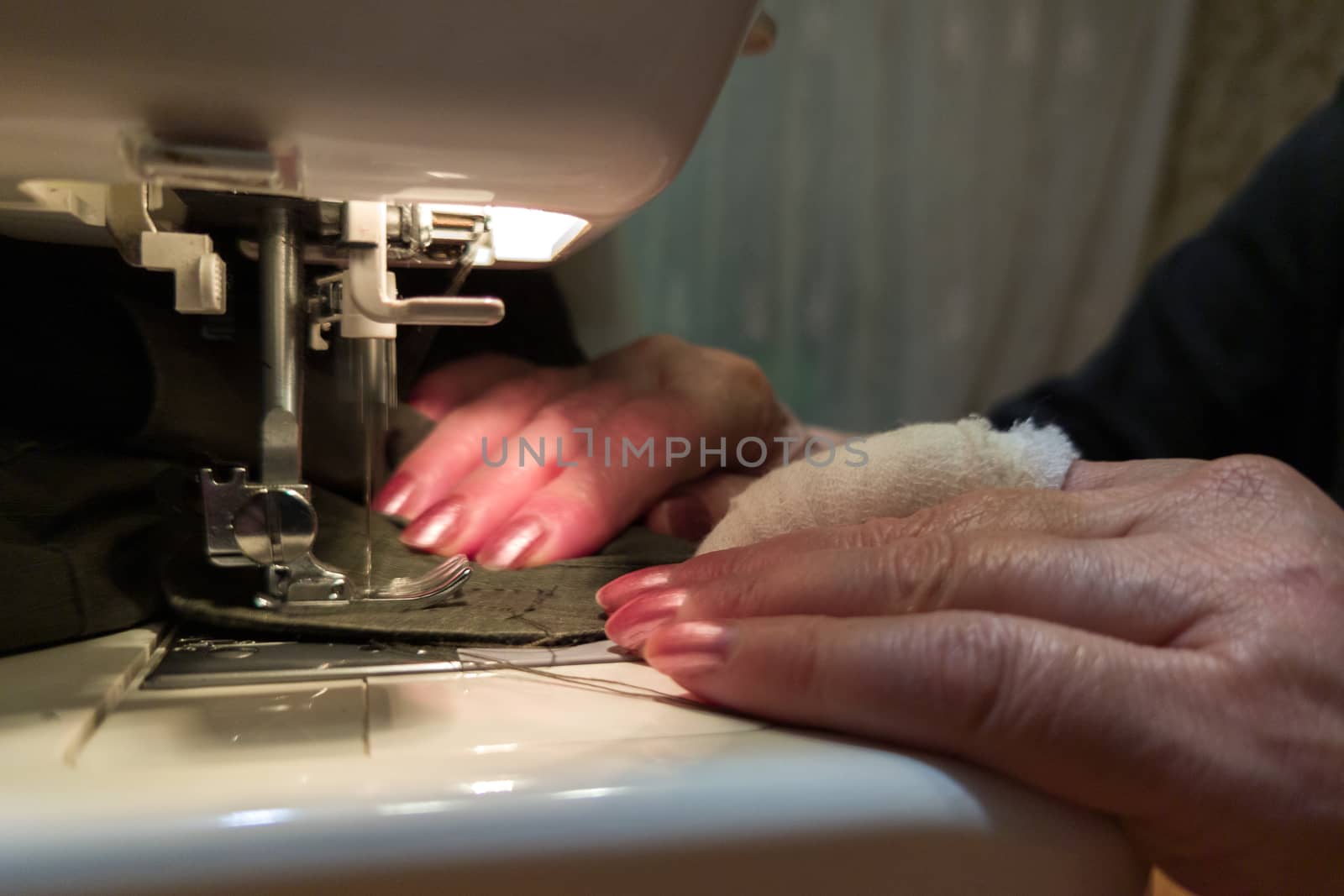 a hand of aged womans with a bandaged finger sews with a sewing machine by z1b