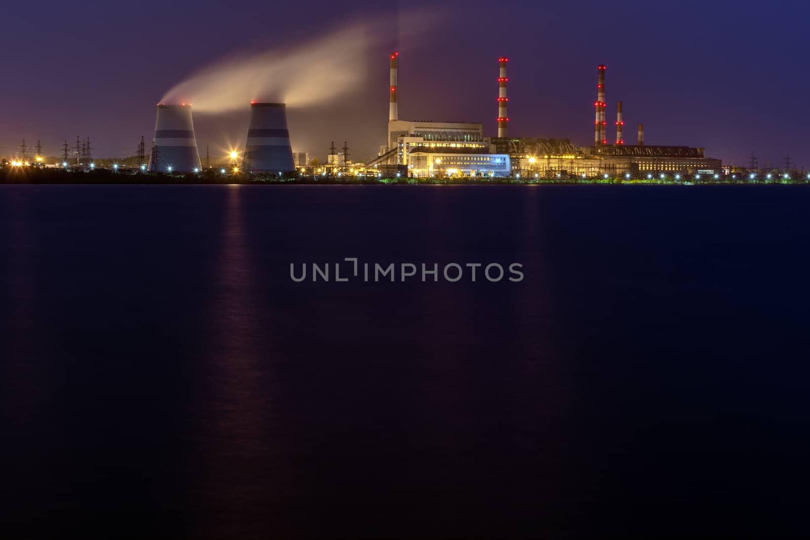 old thermal 450 megawatt power plant at night with artificial lake on foreground.