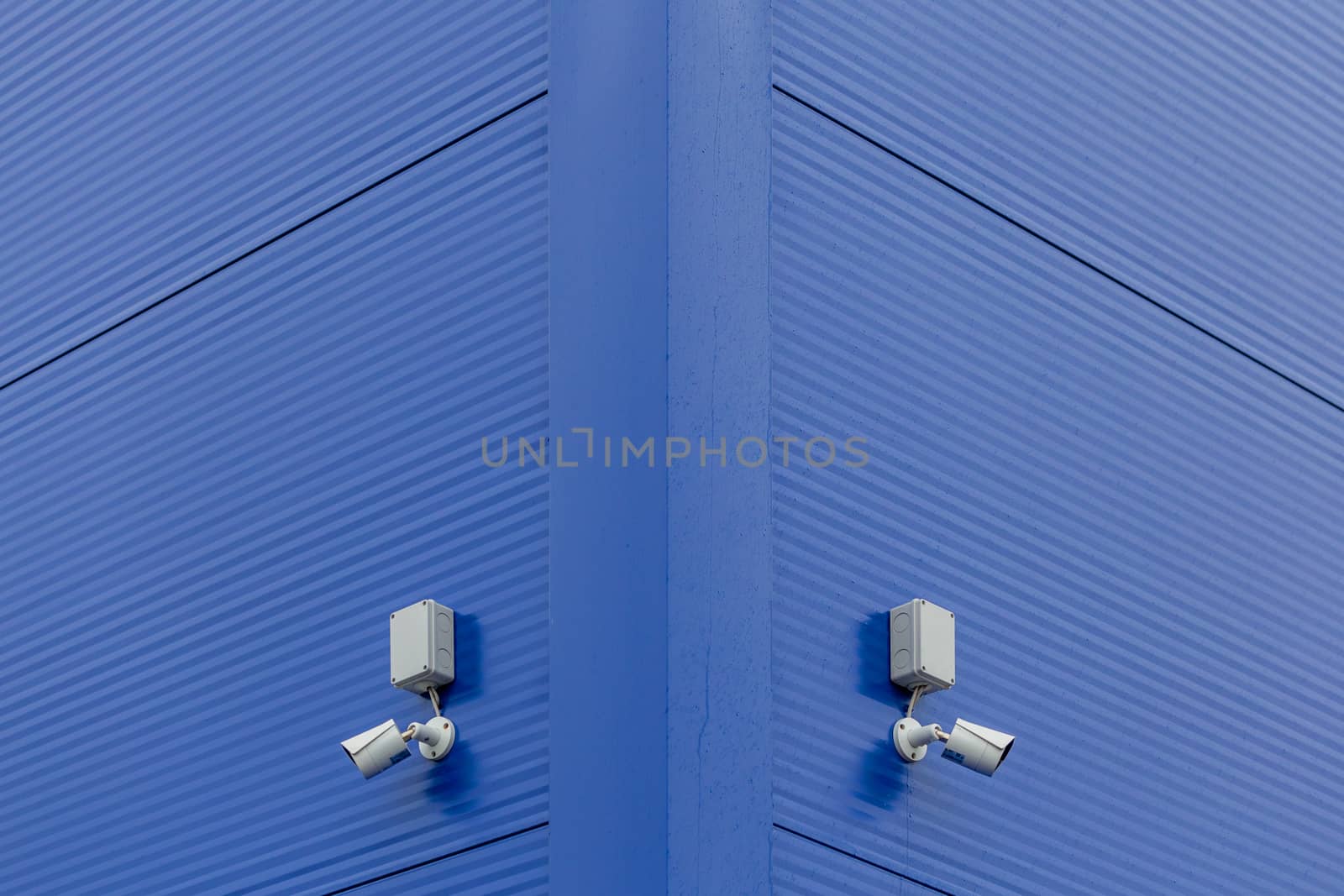 two small white security cameras on blue steel building corner.
