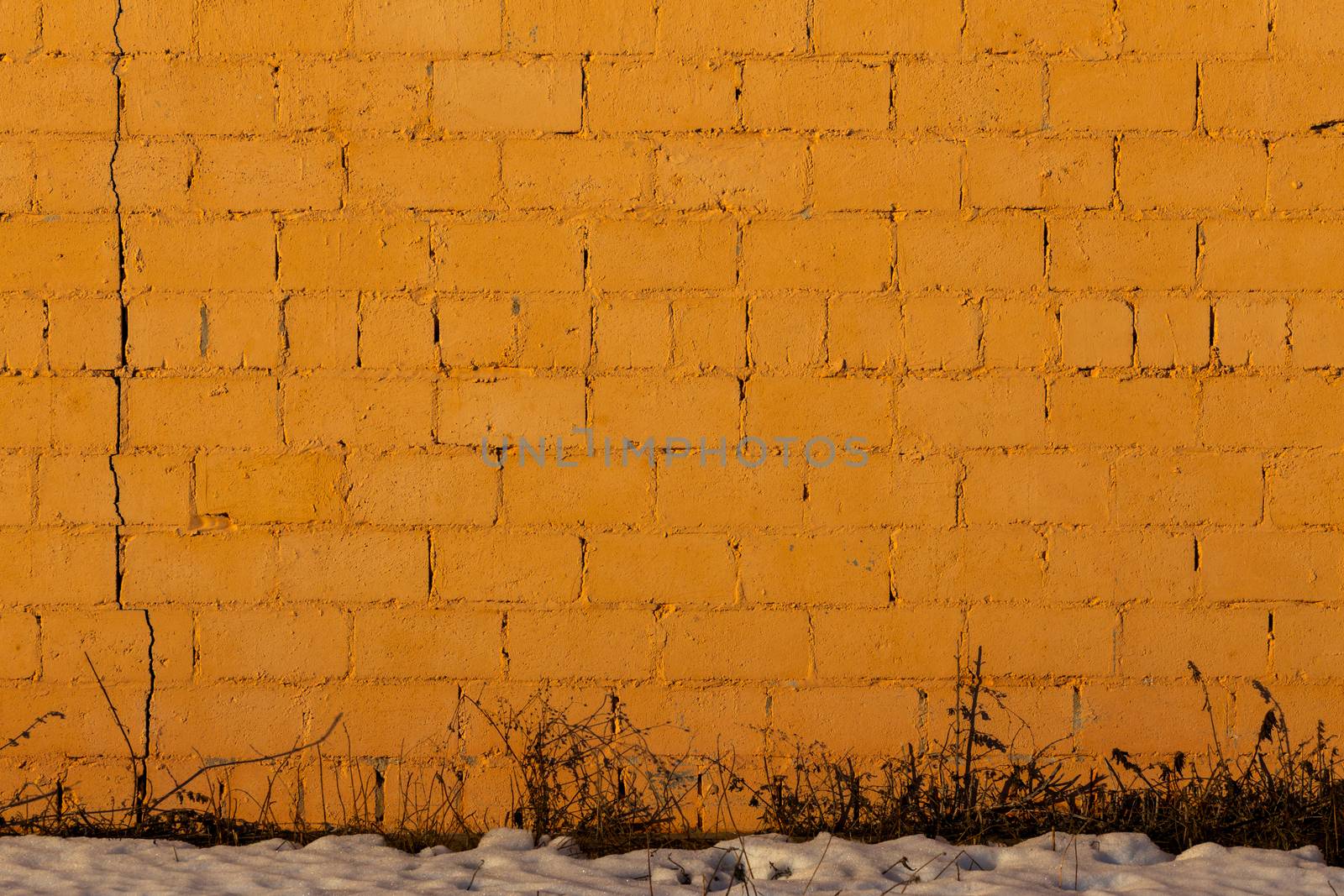 orange plaster rough brick wall texture under direct sunlight with snow and dry gasss under