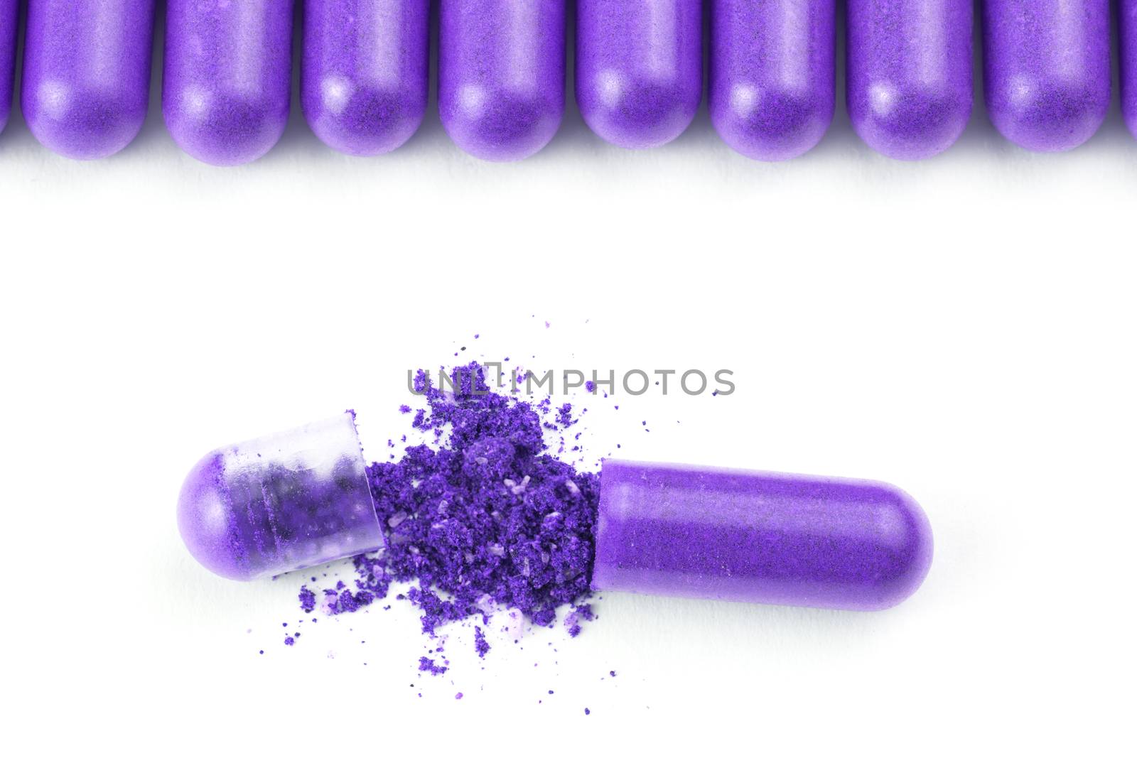 row of proton purple color organic capsules isolated on white background closeup with one opened.