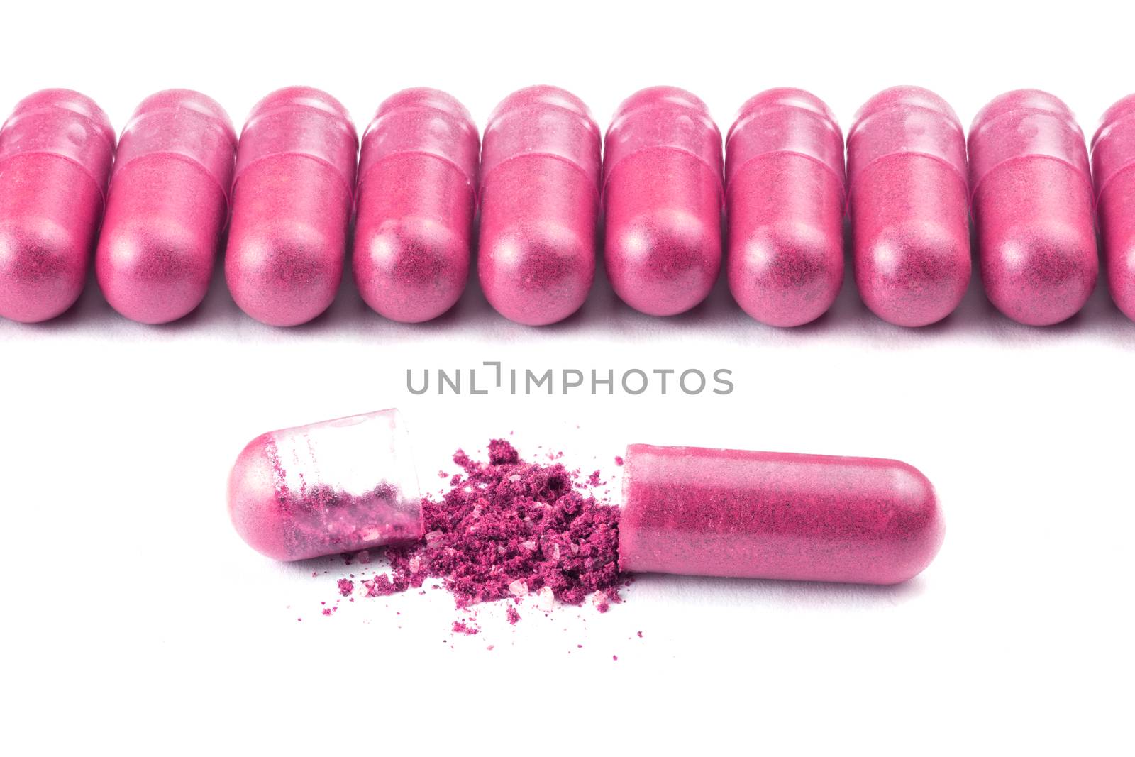 row of plastic pink color organic capsules isolated on white background closeup with one opened.